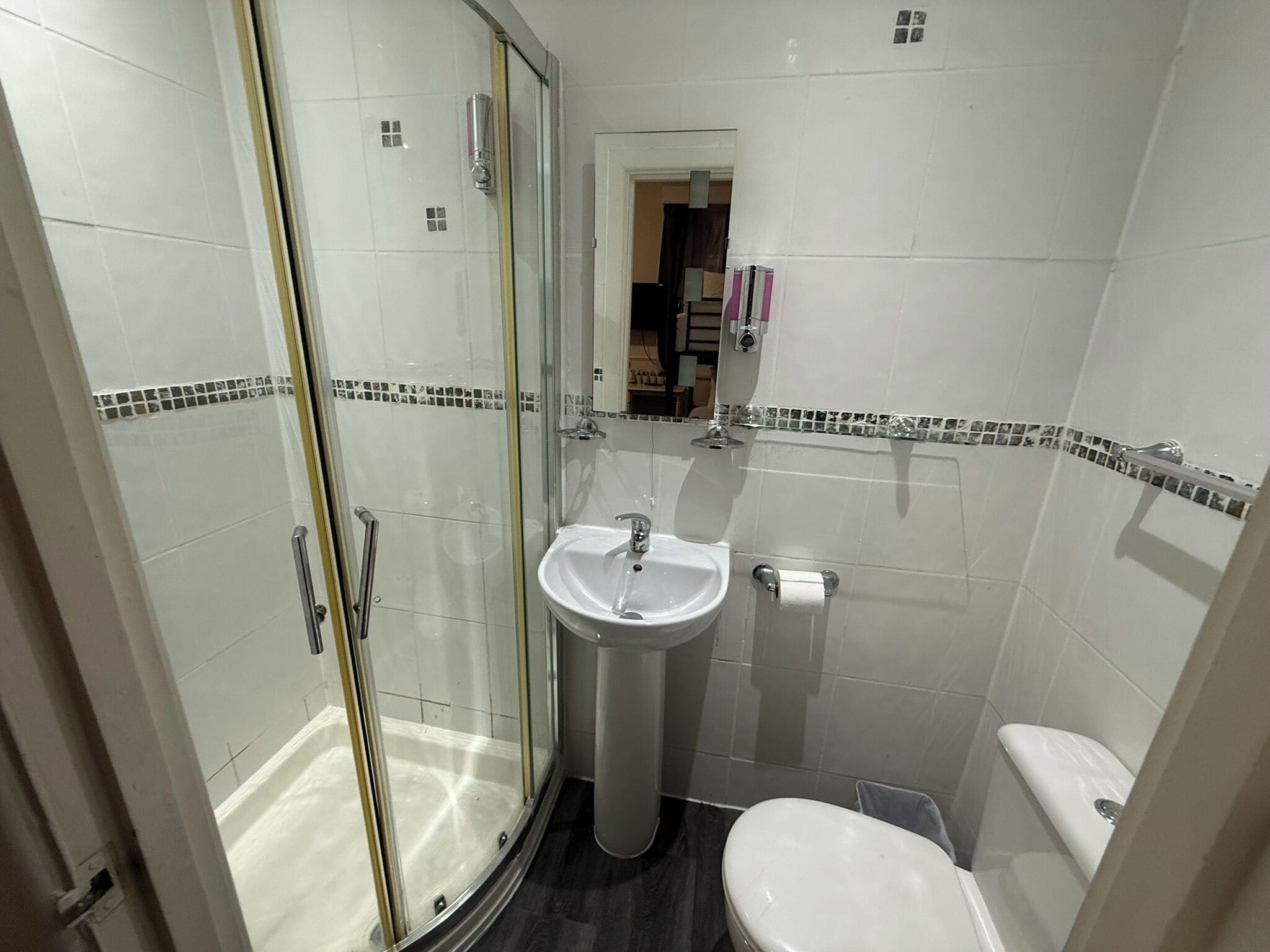 A bathroom with a glass shower enclosure, a pedestal sink, and a toilet.