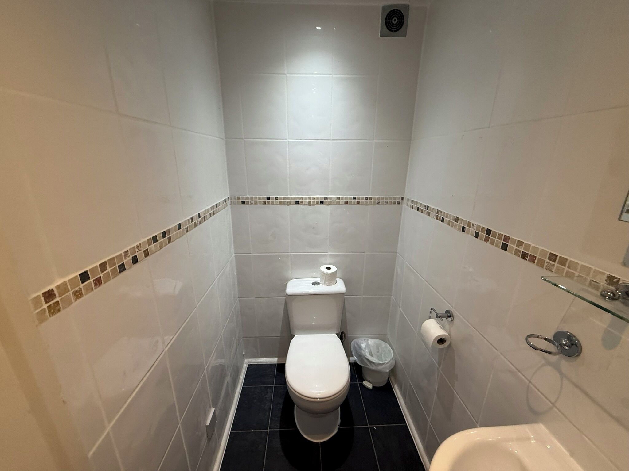 A small, tiled bathroom with a toilet, a trash bin, and a glass shower enclosure.