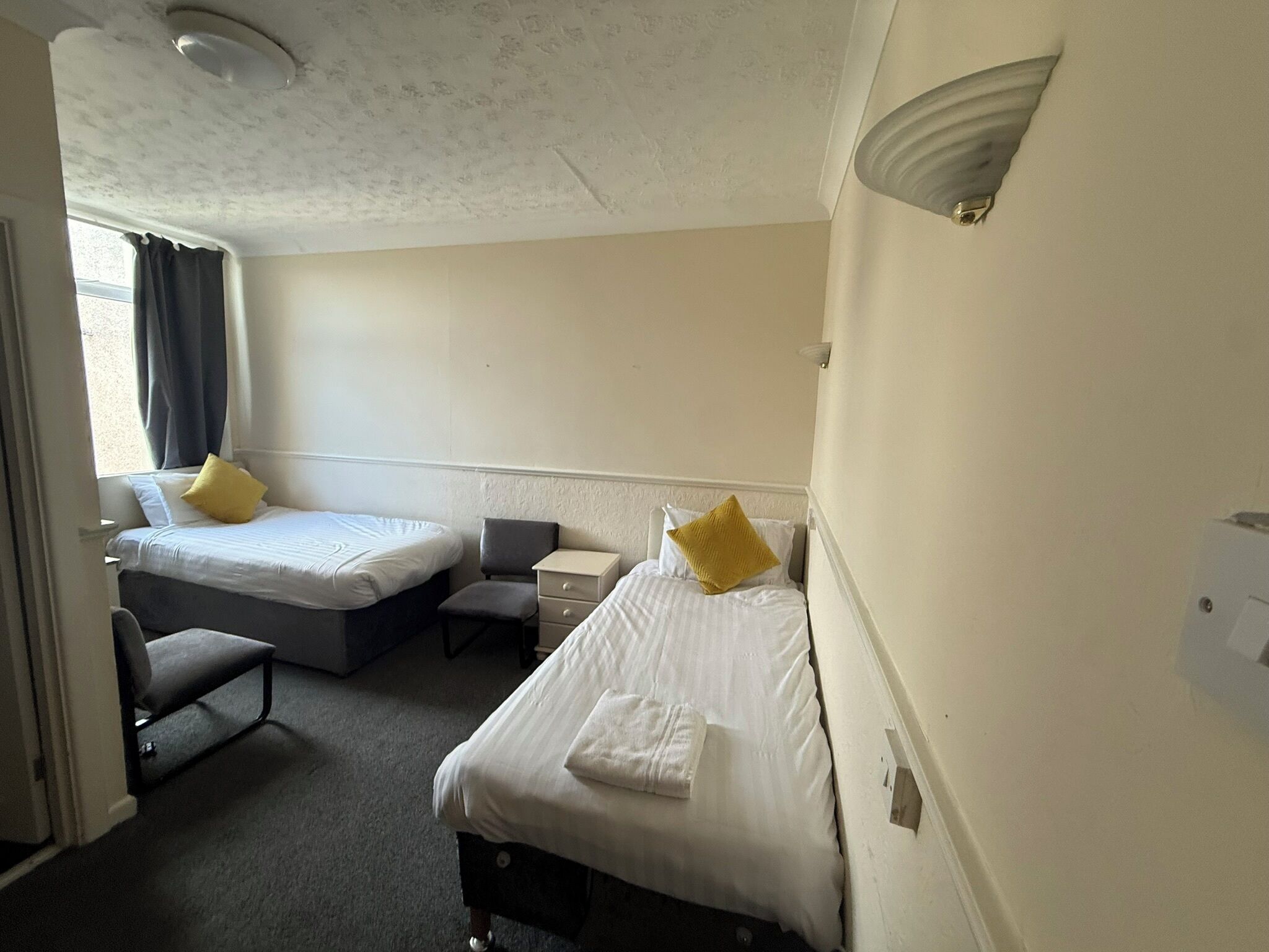 A hotel room with two beds, a small desk, a chair, and a window with curtains.