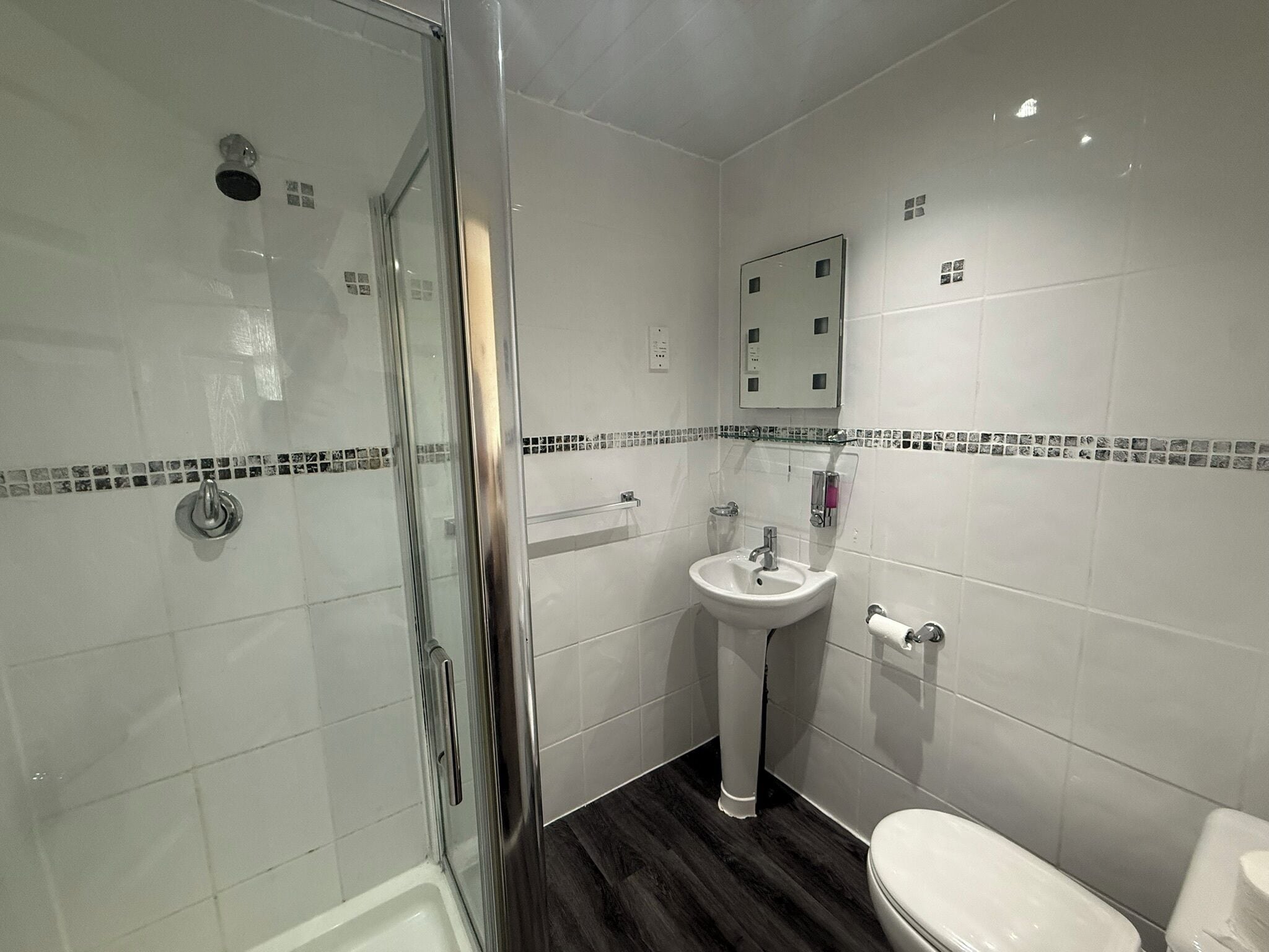 A bathroom with a glass shower enclosure, a pedestal sink, and a toilet.