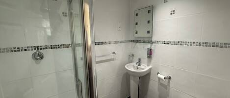 Een badkamer met een douchecabine van glas, een wastafel op een voetstuk en een toilet.