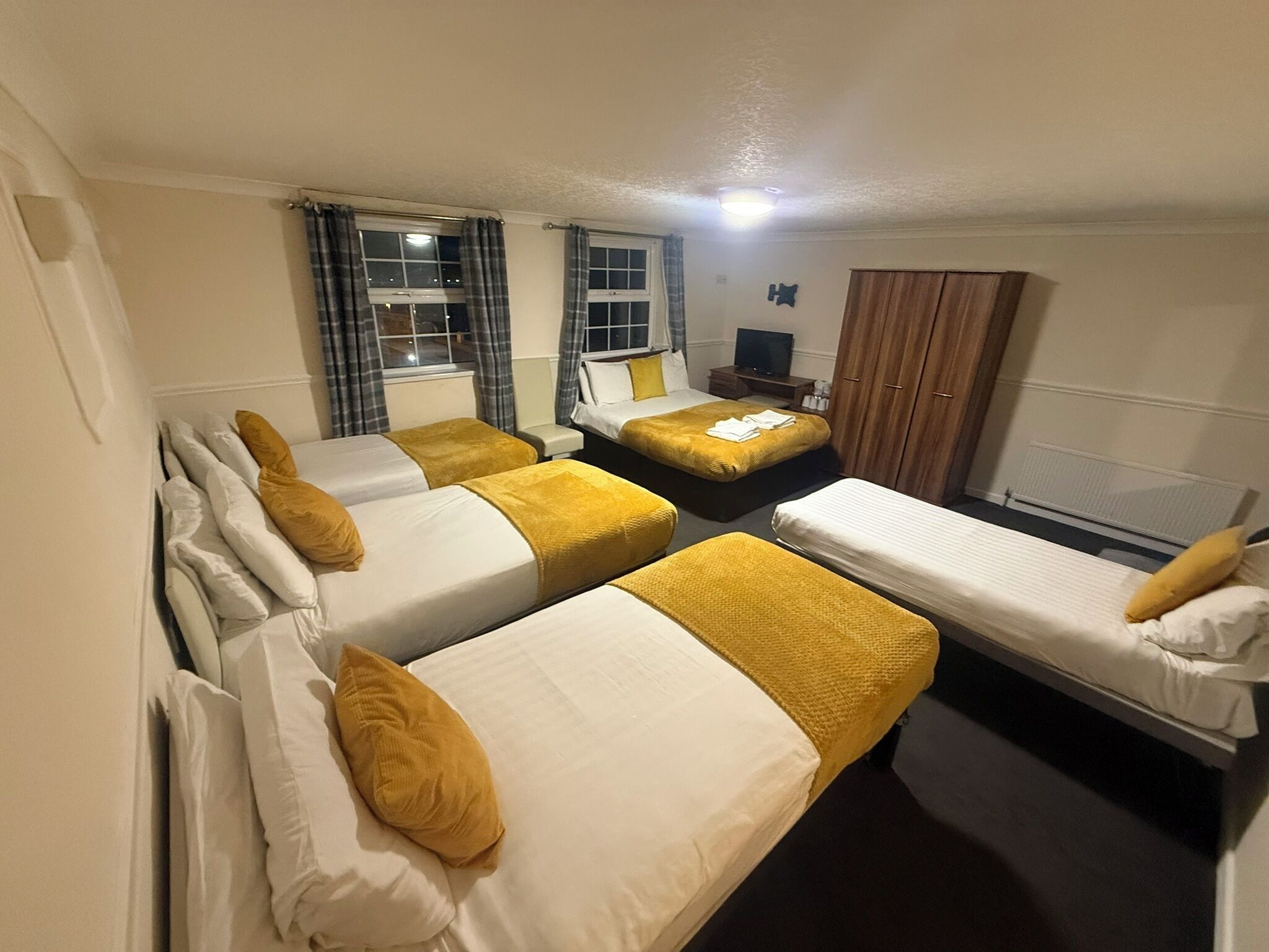 A hotel room with four single beds, a television, a wardrobe, and a window with curtains.