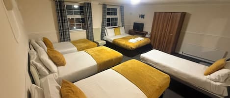 Una habitación de hotel con cuatro camas individuales, televisión, armario y ventana con cortinas.