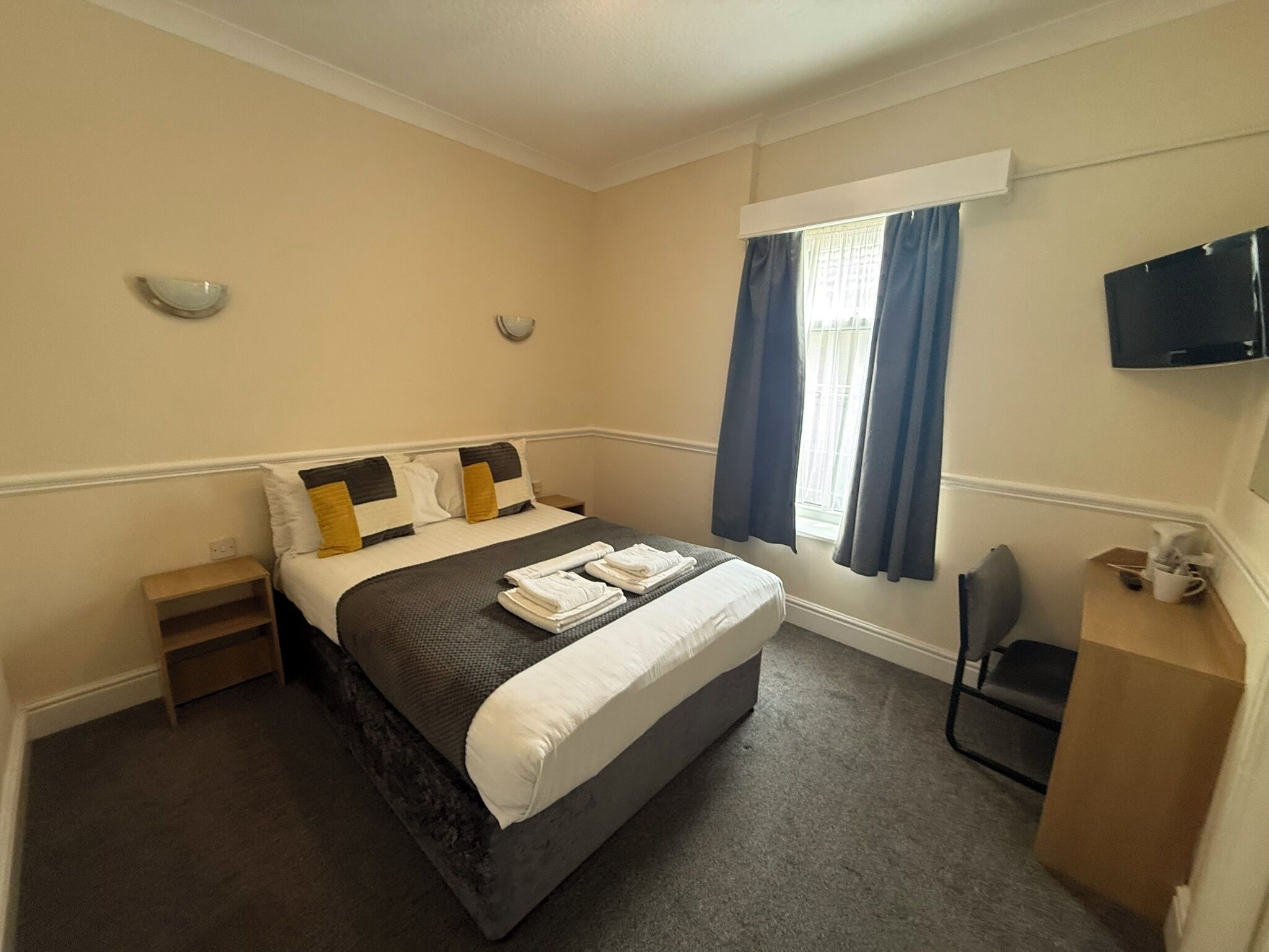 A bedroom with a bed, a nightstand, a chair, a television, and a window with curtains.