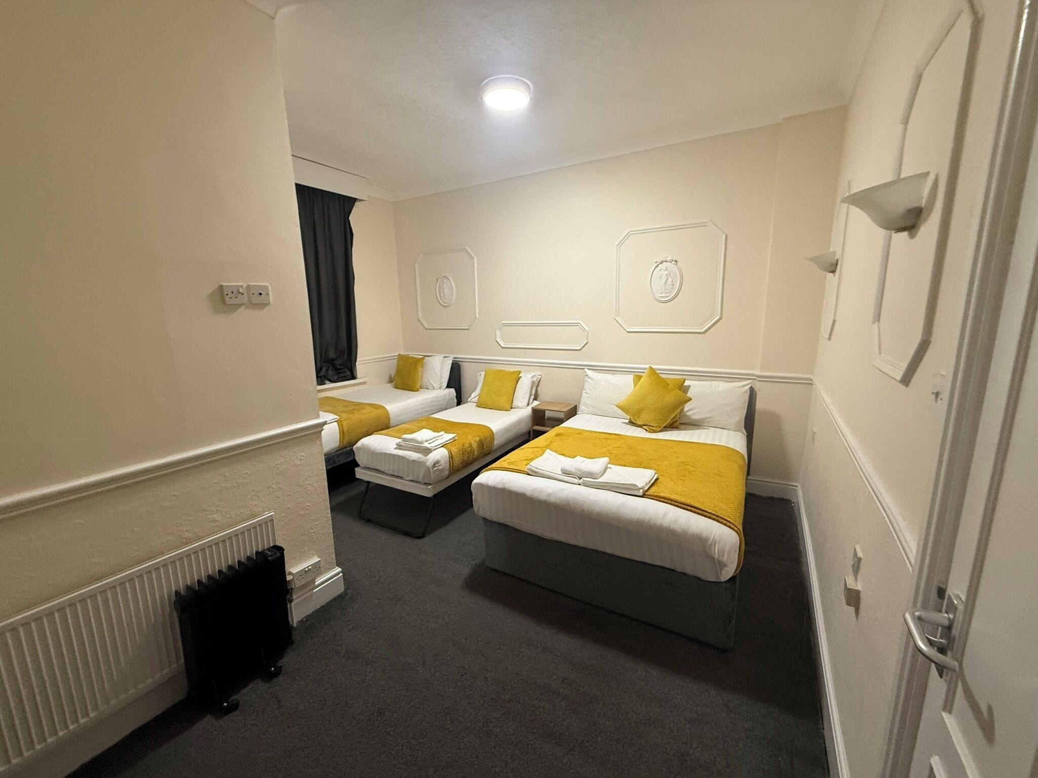 Een hotelkamer met twee bedden, een radiator, een raam met gordijnen en een deur.