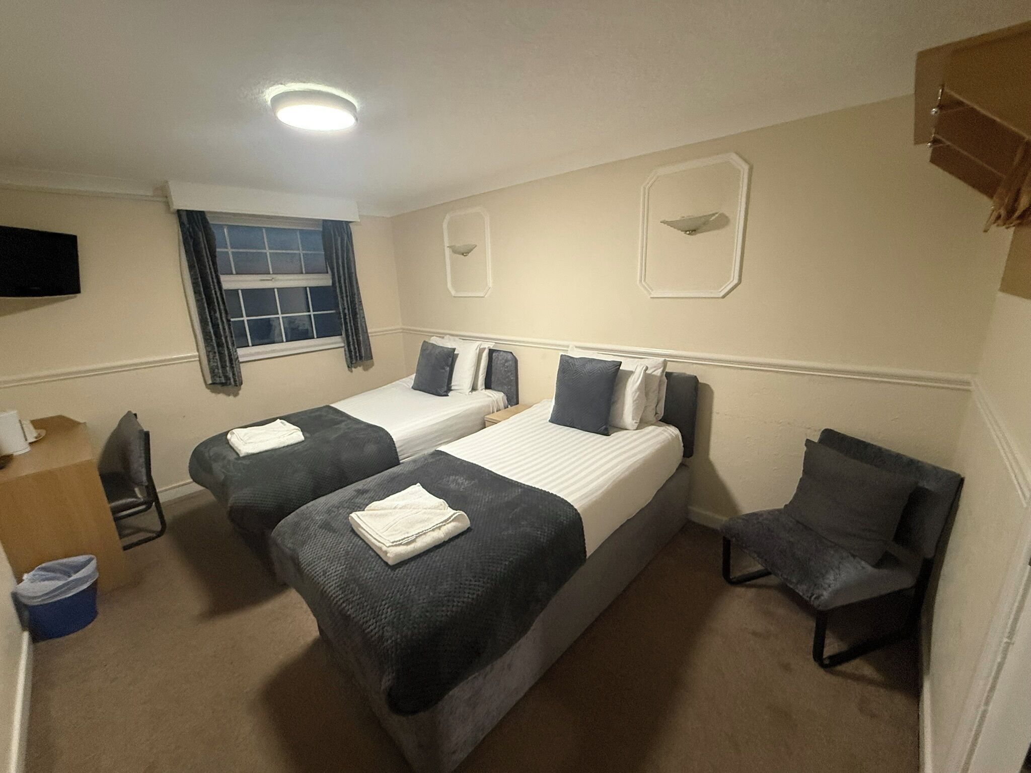 A hotel room with two beds, a desk, a chair, a TV, and a window with curtains.