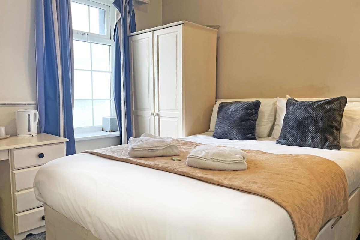 Una habitación de hotel con cama, mesita de noche, armario y ventana con cortinas.