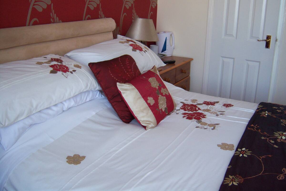 Una cama bien hecha con ropa de cama floral y un cojín rojo y beige.
