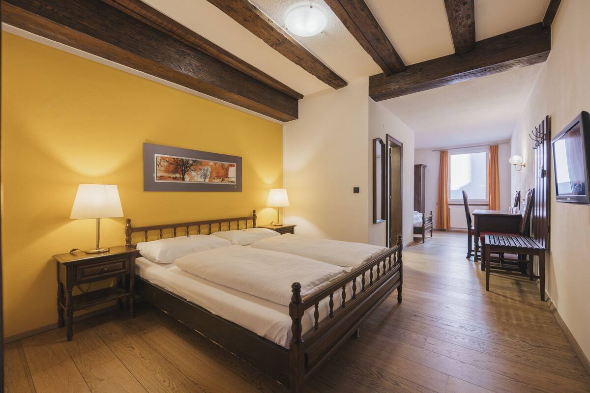 Une chambre avec un lit en bois, deux tables de chevet avec des lampes, un tableau au mur et un banc en bois dans un coin.