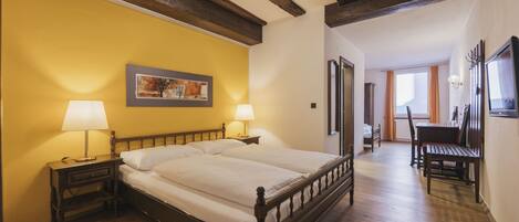 A bedroom with a wooden bed, two bedside tables with lamps, a painting on the wall, and a wooden bench in the corner.