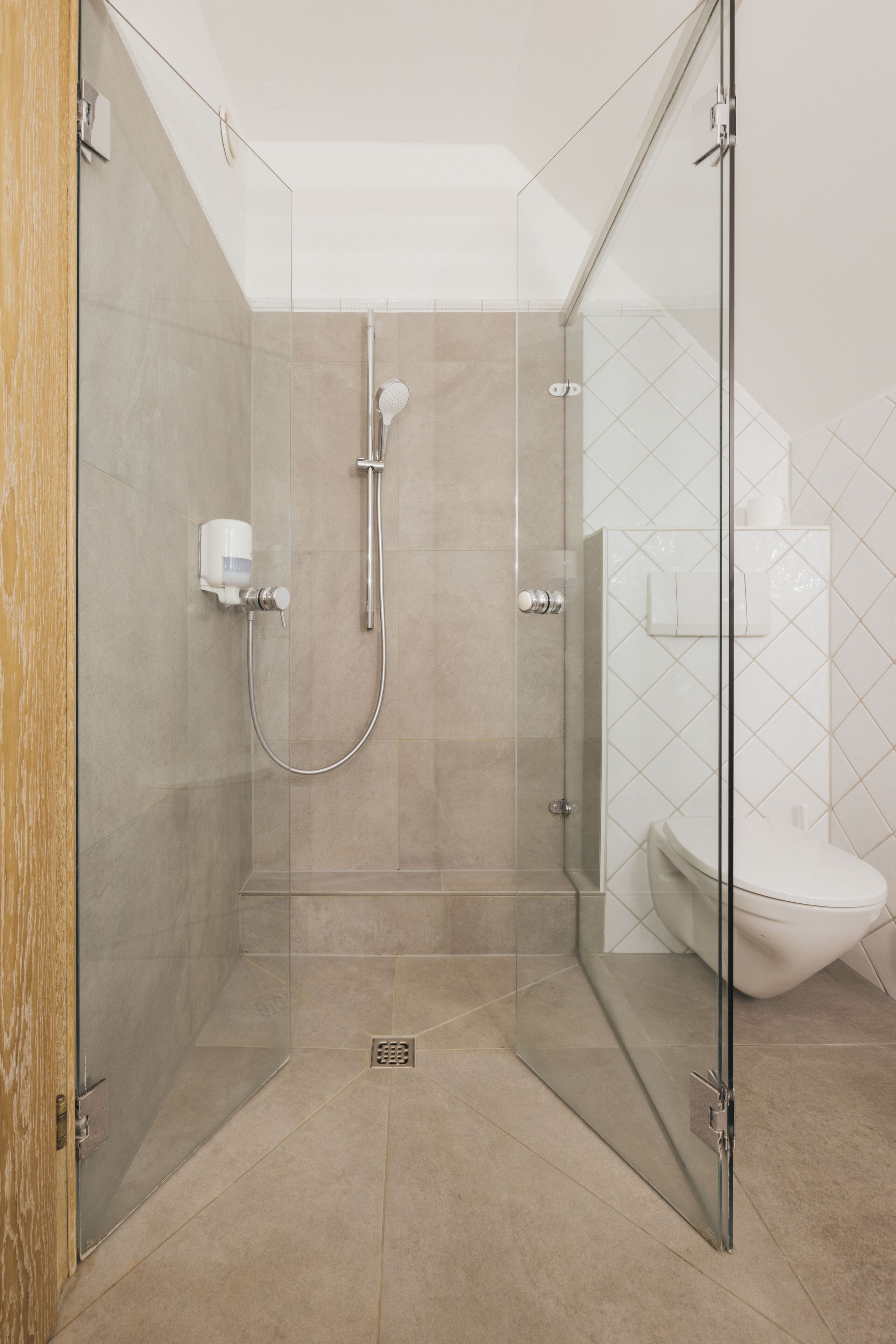 A modern bathroom with a glass-enclosed shower, a toilet, and a towel dispenser.