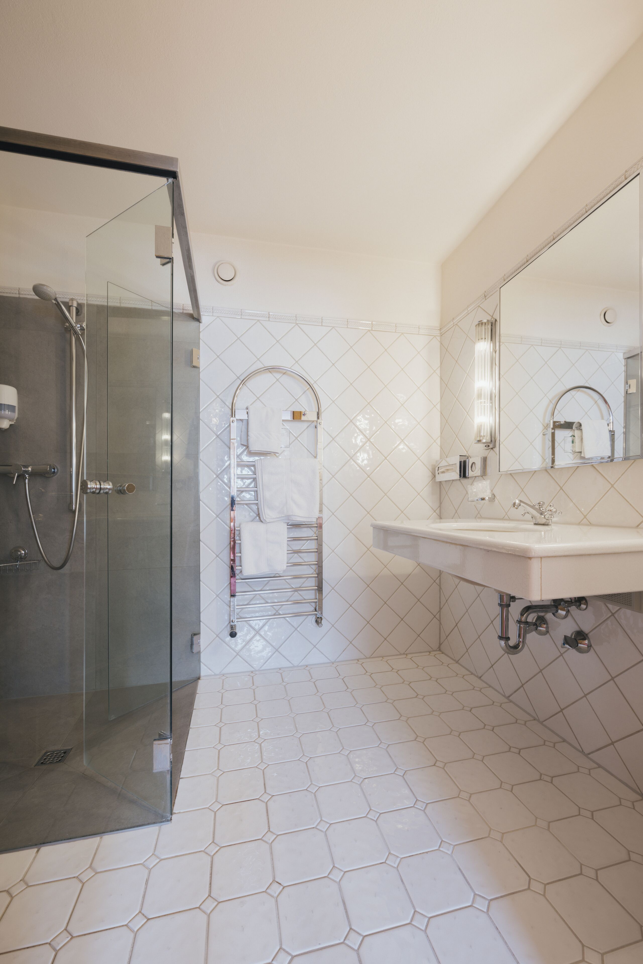 A modern bathroom with a glass-enclosed shower, a sink with a mirror, and a tiled floor.