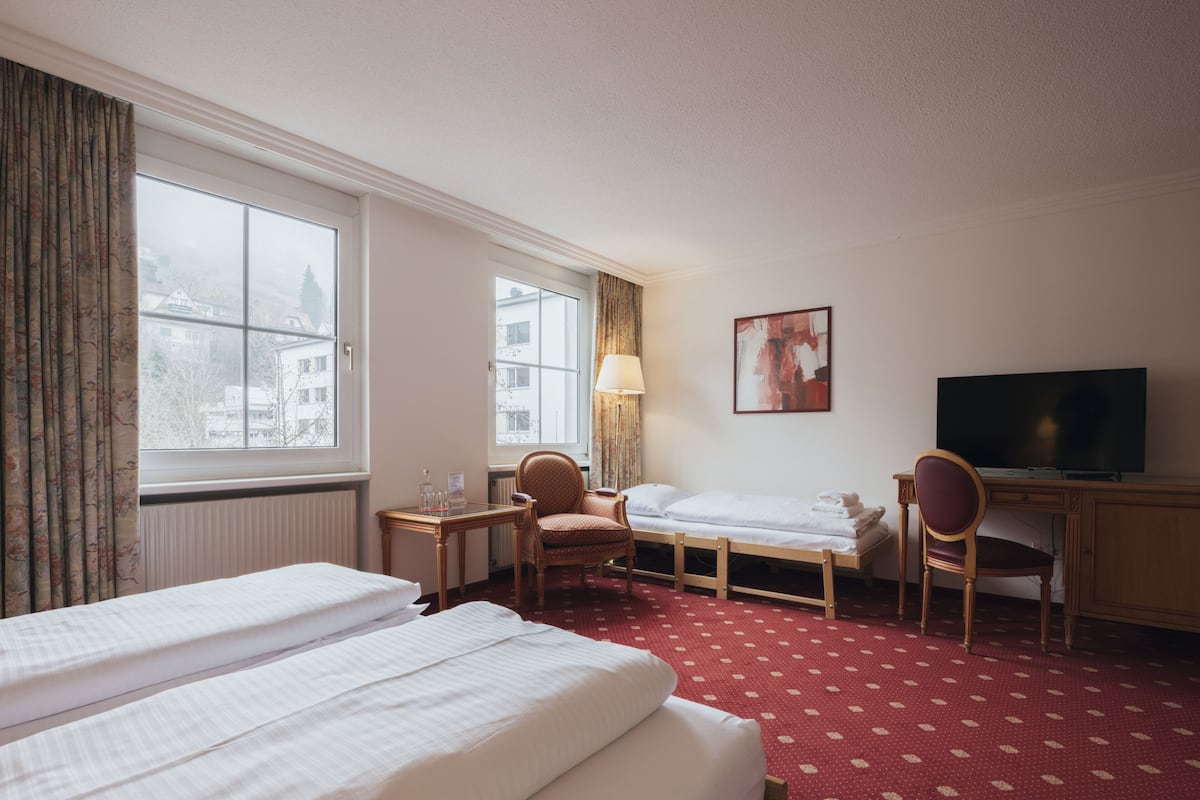 Une chambre d’hôtel avec un grand lit, un bureau, une chaise, une télévision et une fenêtre avec des rideaux.