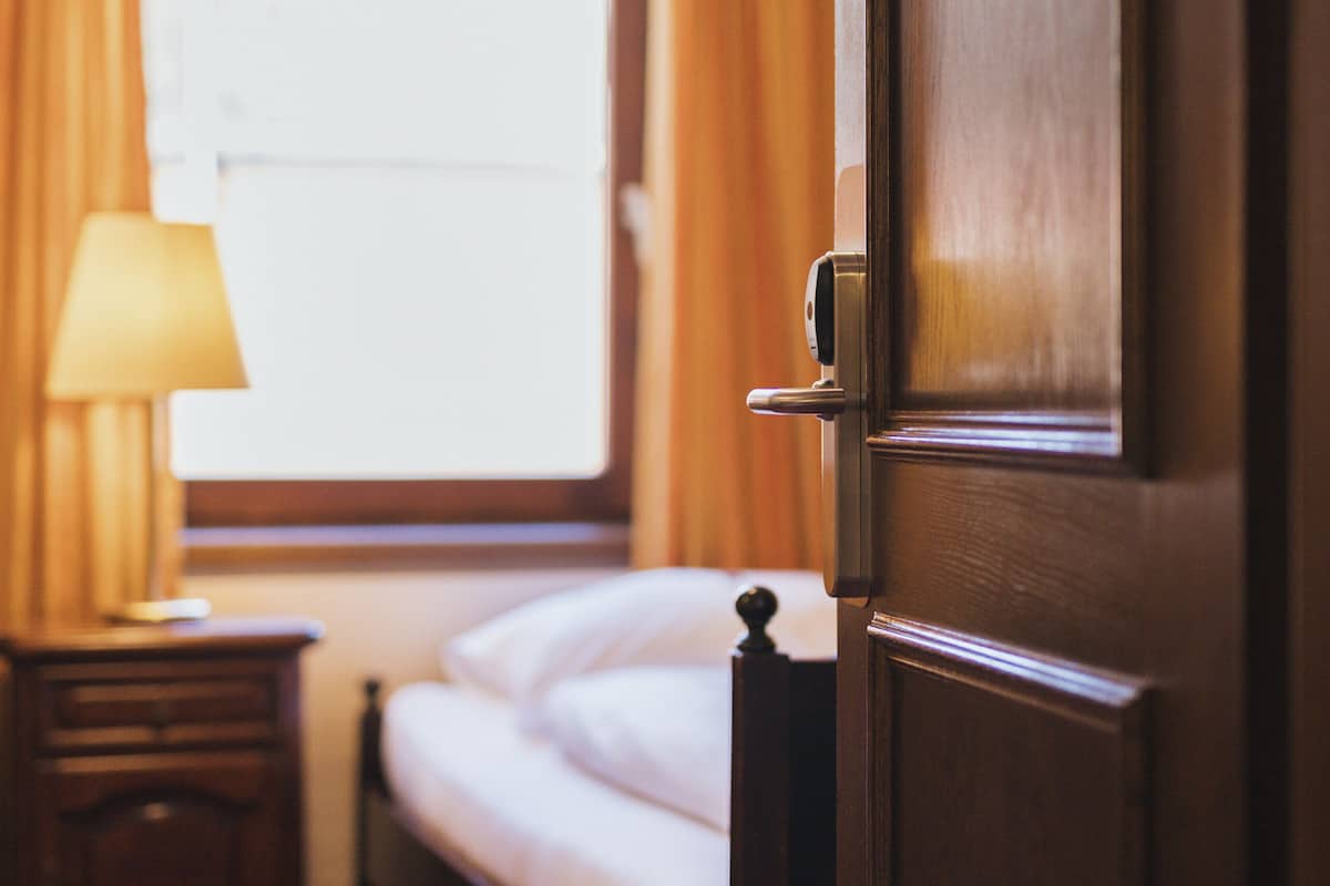 Une chambre d’hôtel avec un lit, une table de chevet avec une lampe et une fenêtre avec des rideaux.