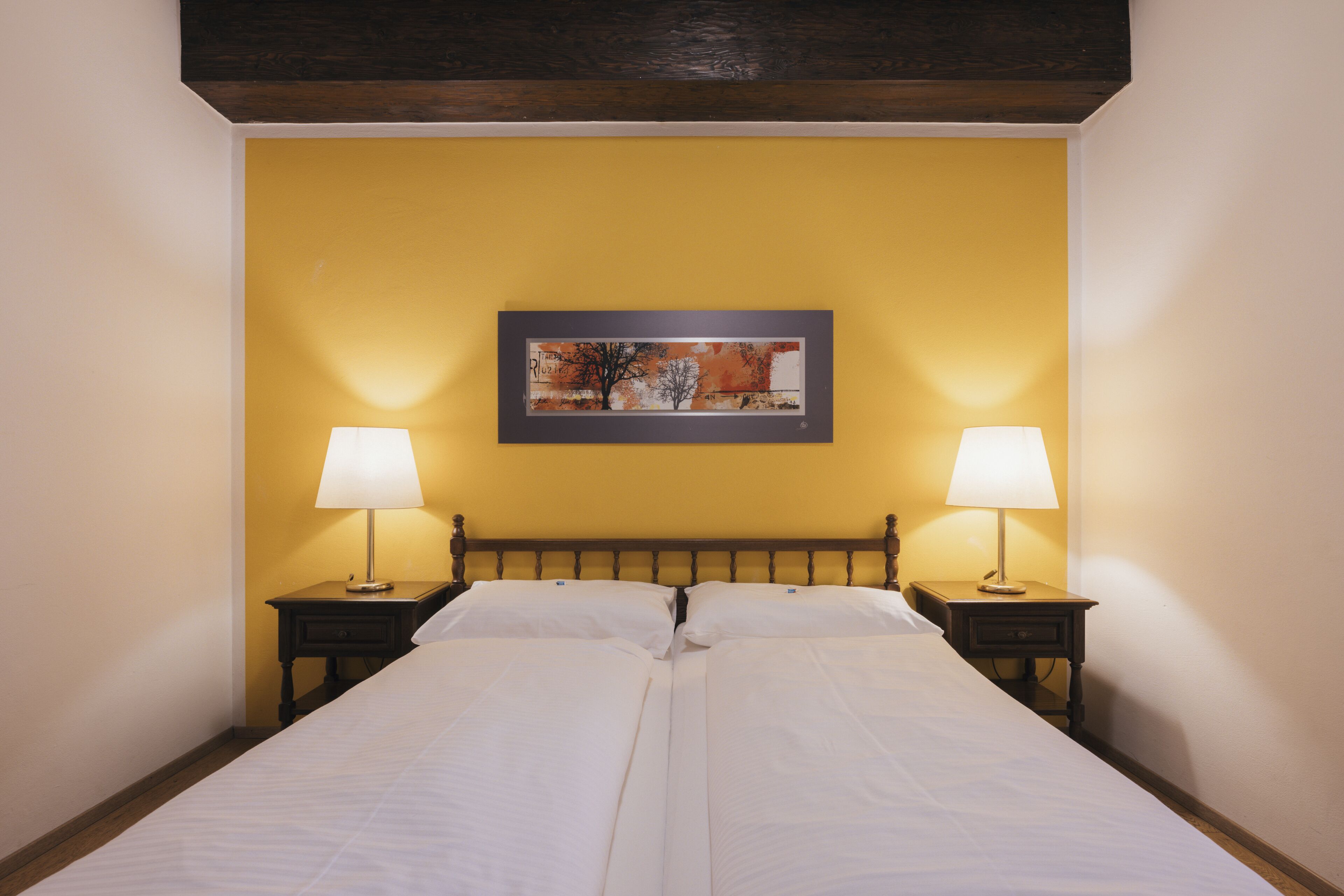 A neatly made bed with white linens, two bedside tables with lamps, and a framed picture on the wall.