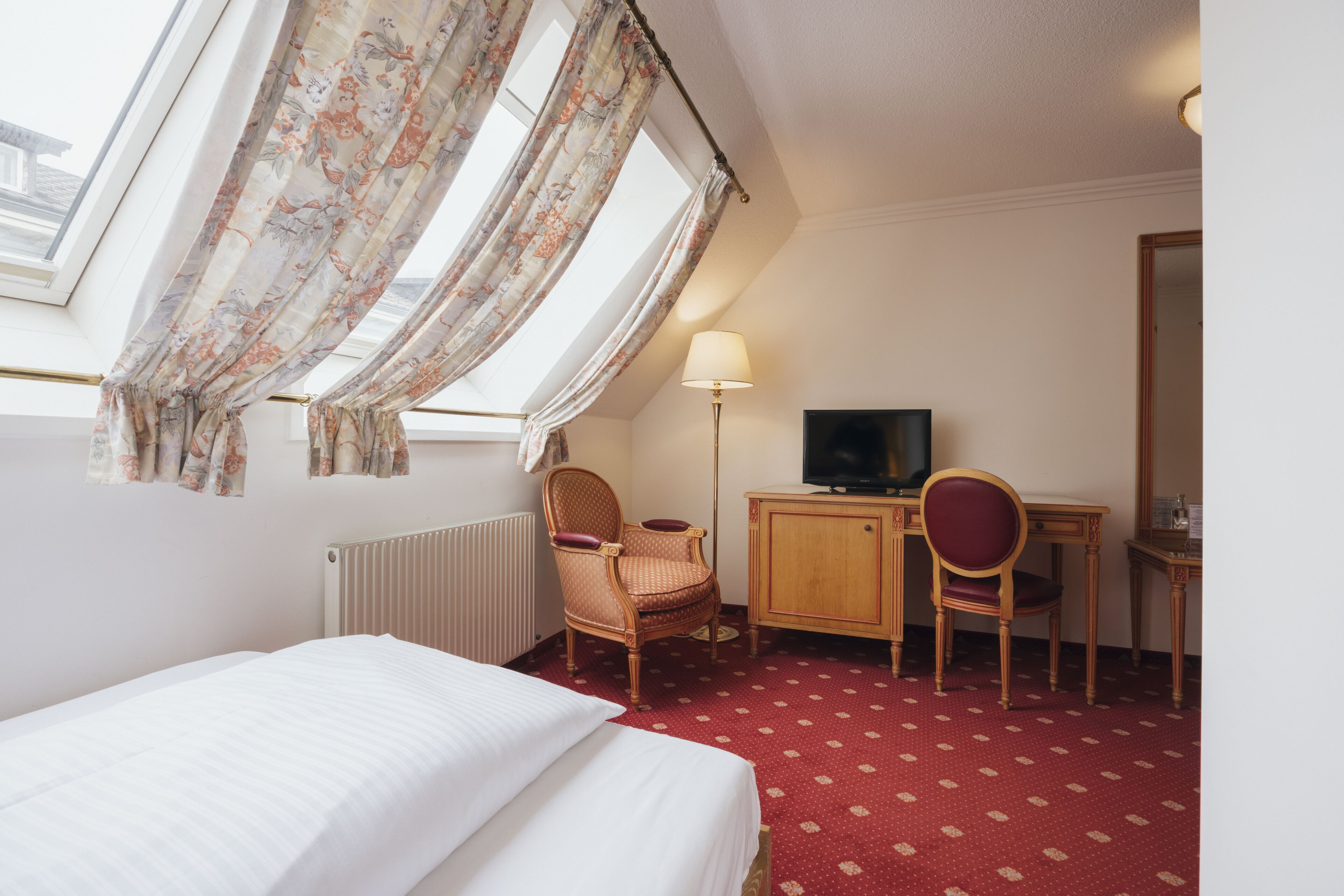 A hotel room with a bed, a desk, a chair, a television, and a window with curtains.