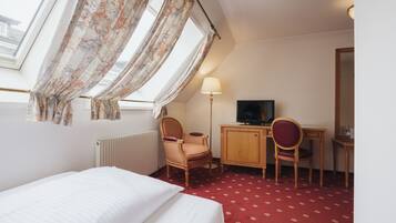 A hotel room with a bed, a desk, a chair, a television, and a window with curtains.