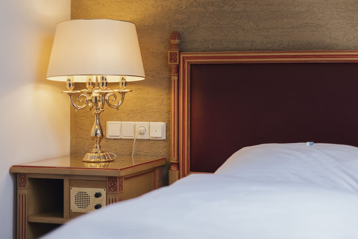 Une chambre d’hôtel avec un lit, une table de chevet avec une lampe et un interrupteur au mur.
