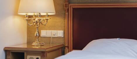 A hotel room with a bed, a bedside table with a lamp, and a wall switch.