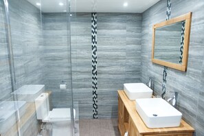 A modern bathroom with a glass shower enclosure, two white sinks, and a wooden vanity.