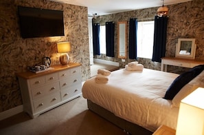 A bedroom with a bed, a dresser, a TV, and a window with curtains.