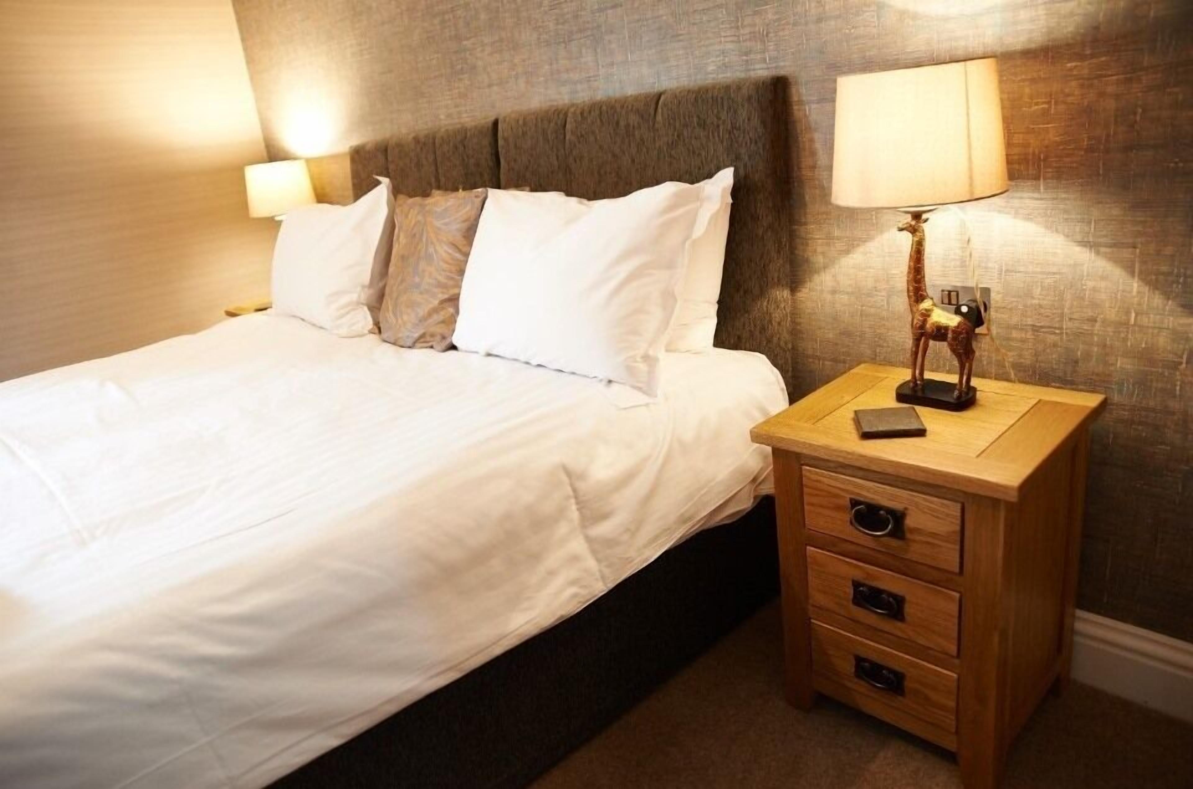 A neatly made bed with white linens, a wooden nightstand with drawers, and a lamp with a giraffe design.