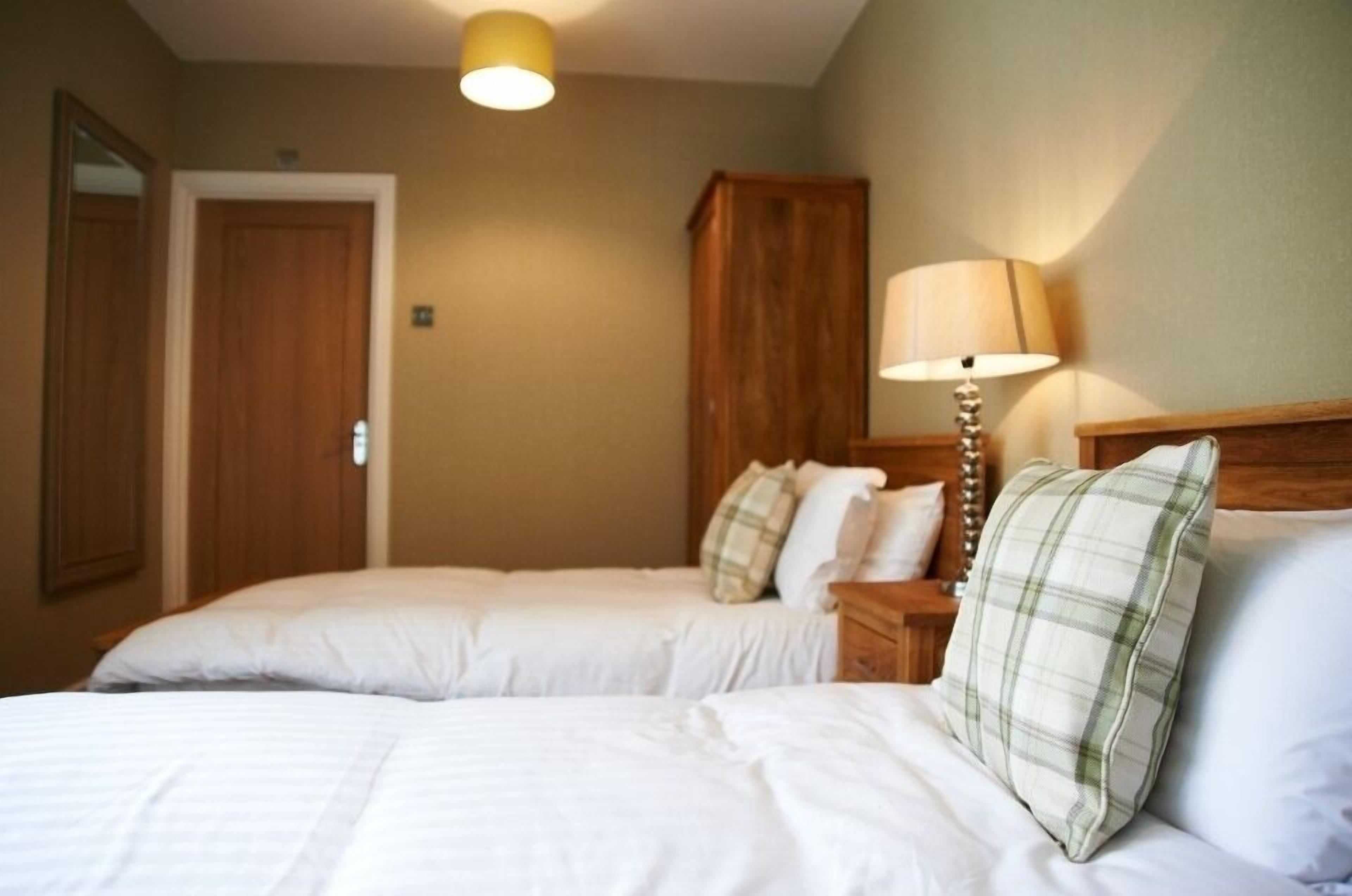 A hotel room with two single beds, a wooden headboard, a bedside lamp, and a mirror on the wall.
