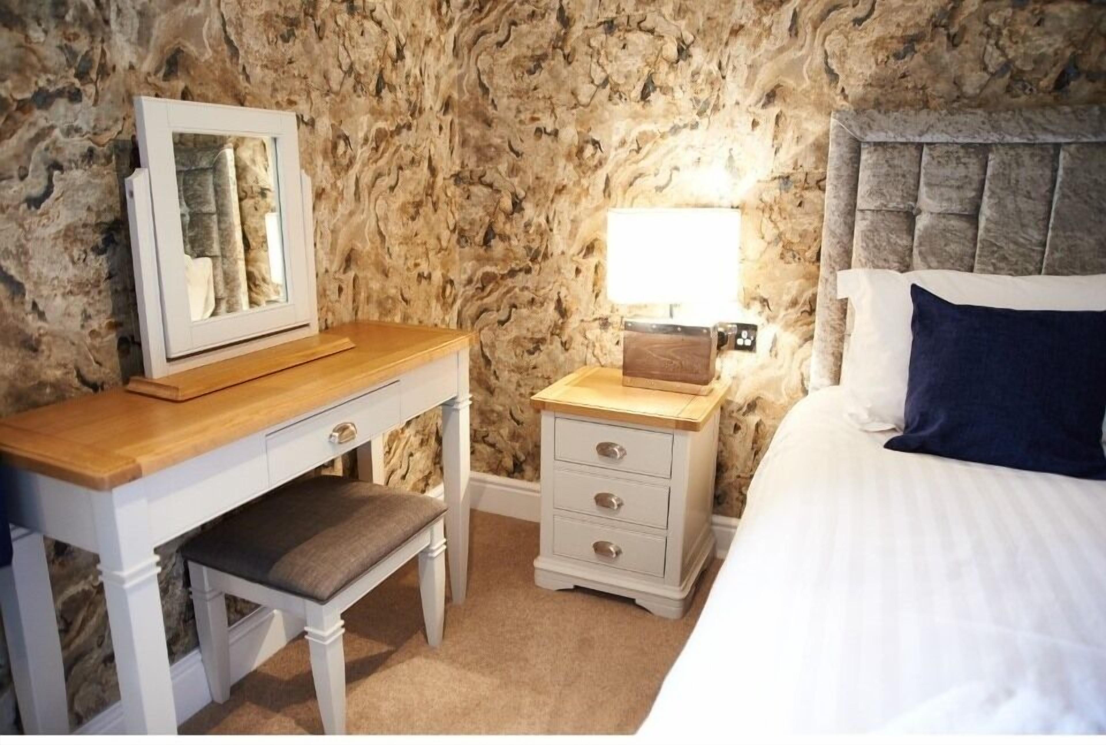 A bedroom with a bed, a bedside table with a lamp, a dresser, and a mirror.