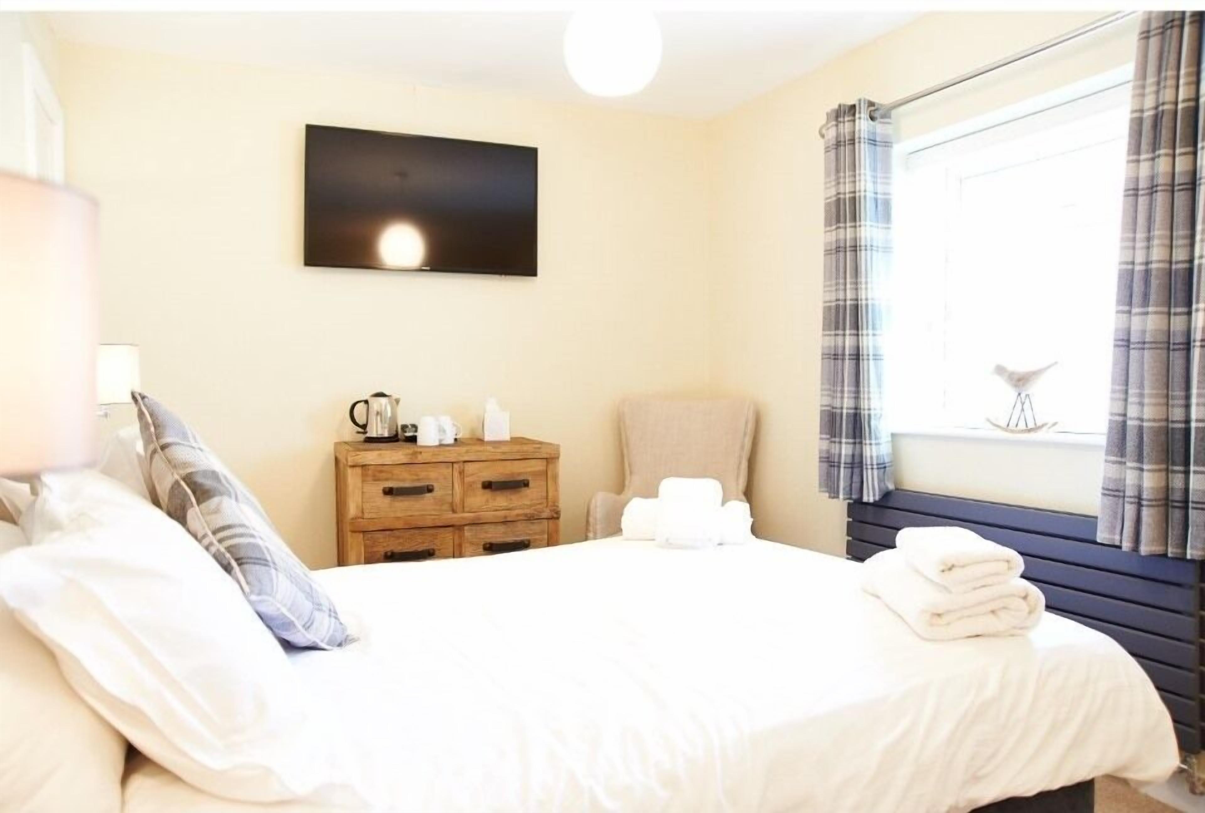 Une chambre d’hôtel comprenant un lit, une table de chevet en bois, une chaise, un téléviseur à écran plat et une fenêtre avec des rideaux.