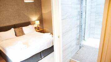 A hotel room with a bed, nightstand, lamp, and a view of a bathroom with a shower and a towel rack.
