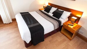 Un lit bien fait, avec une couverture à rayures noires et blanches, une tête de lit en bois et des lampes de chevet.