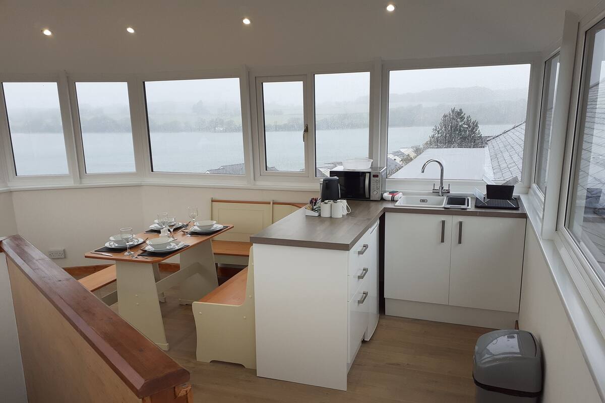 Een moderne keuken met een eetgedeelte, grote ramen en uitzicht op een meer.