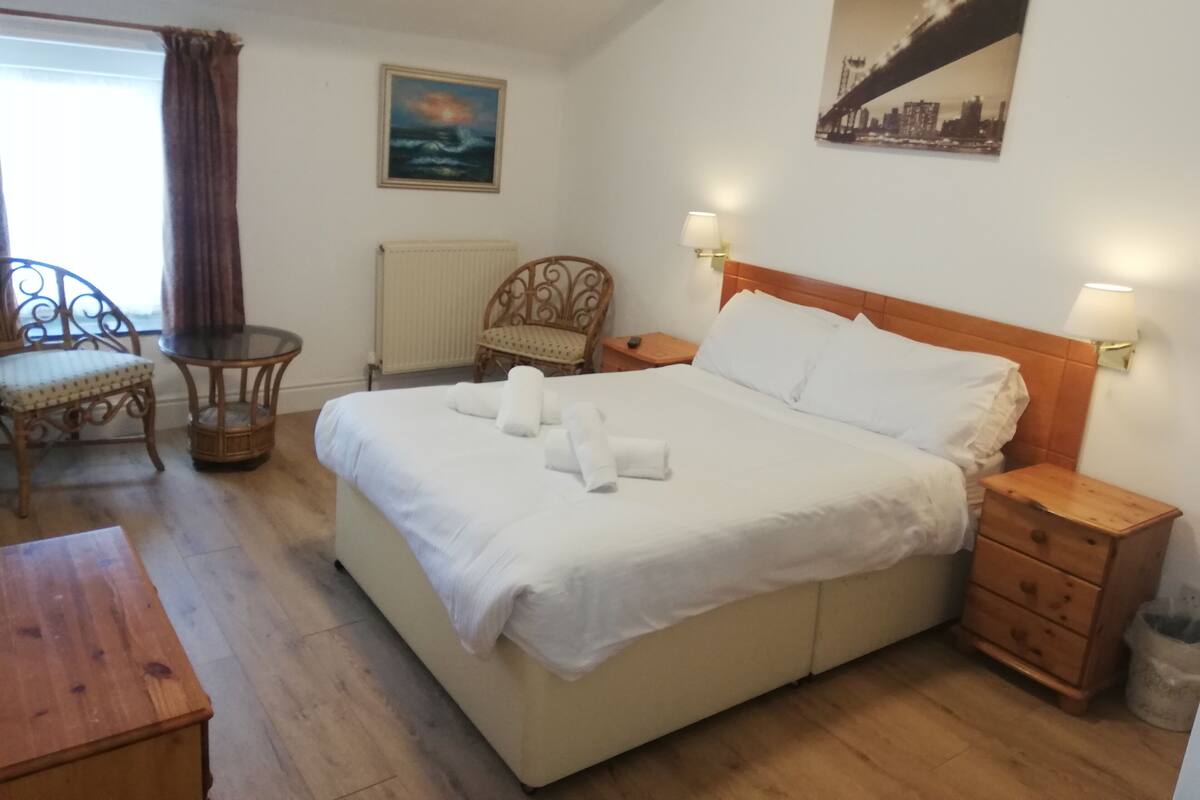 Een keurig opgemaakt hotelkamer met een bed, nachtkastjes, een stoel en een klein tafeltje.