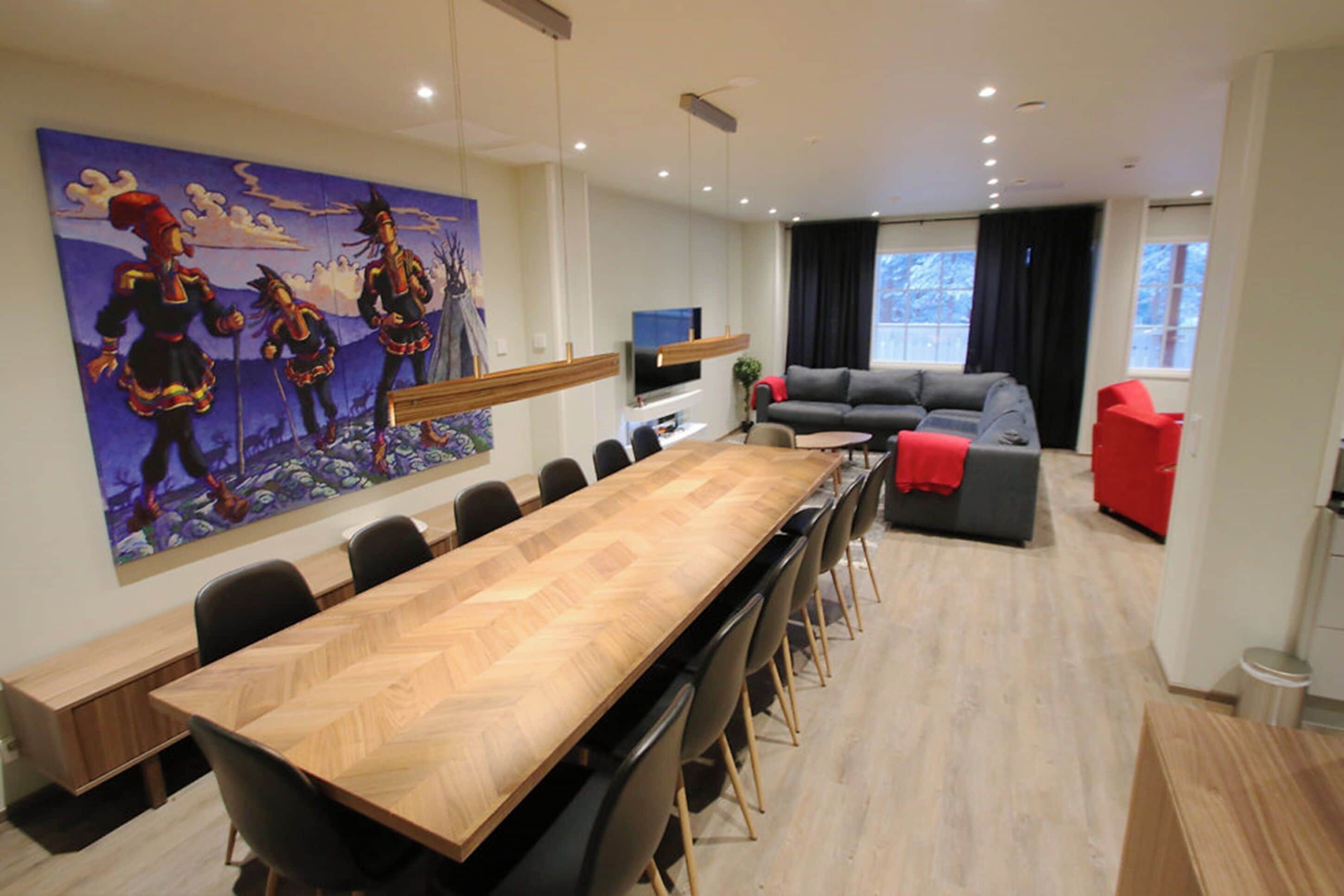 Een moderne vergaderruimte met een lange houten tafel, zwarte stoelen, een grijze bank en een rode fauteuil.