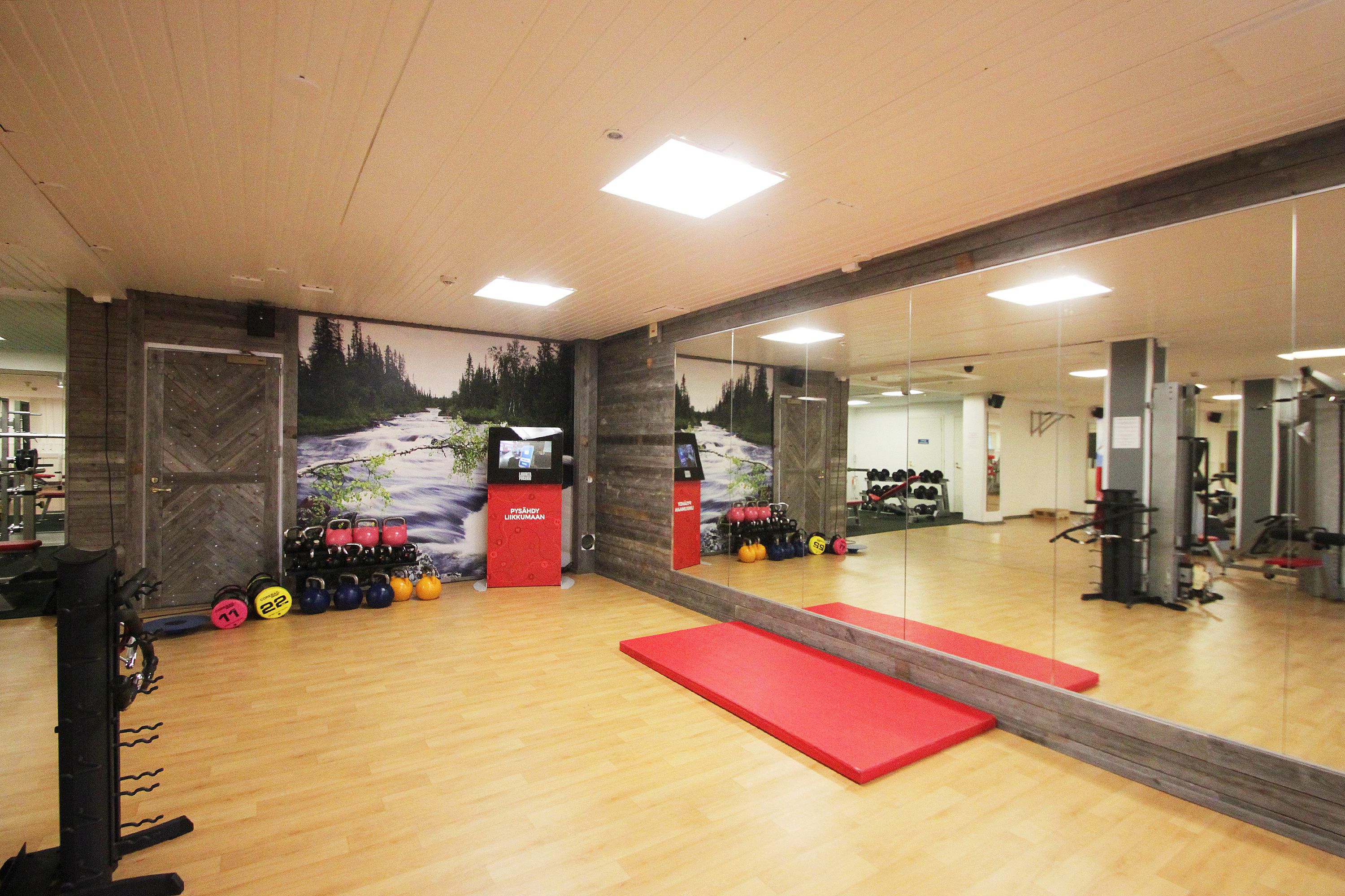A gym with wooden floors, exercise equipment, and a large mirror.