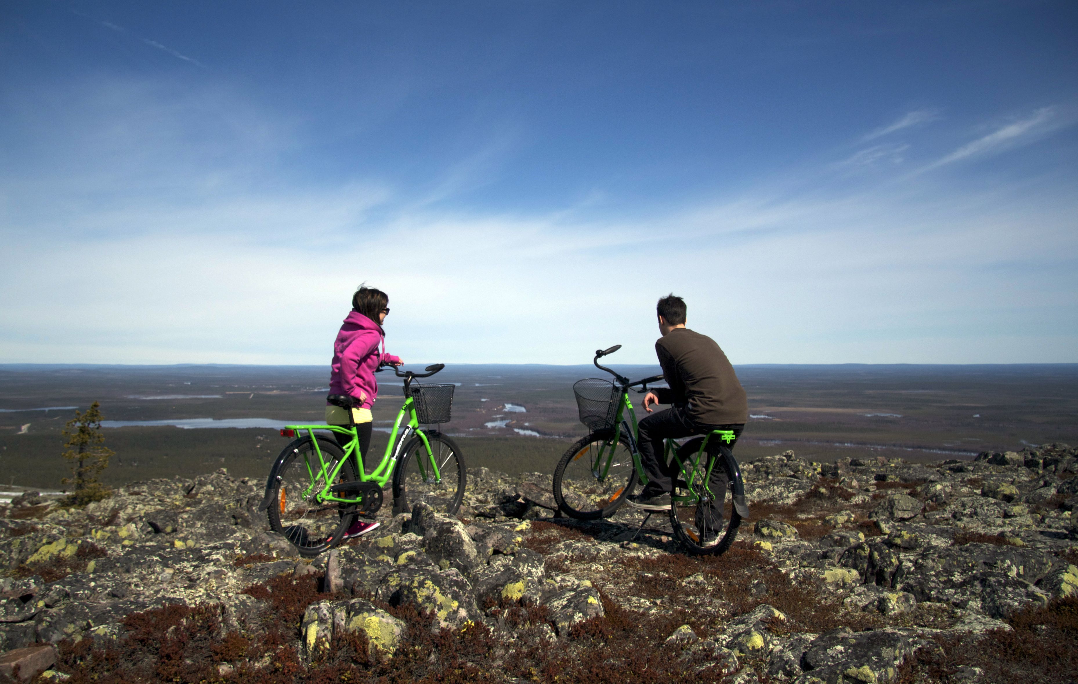 Two people on bicycles on a rocky terrain with a vast landscape in the background.
