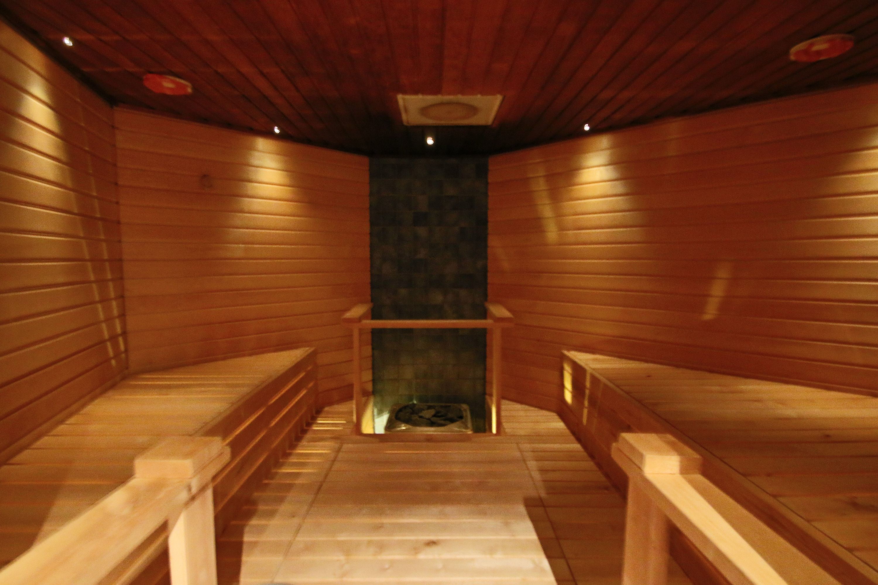 Un sauna avec des bancs en bois et un mur central en pierre.