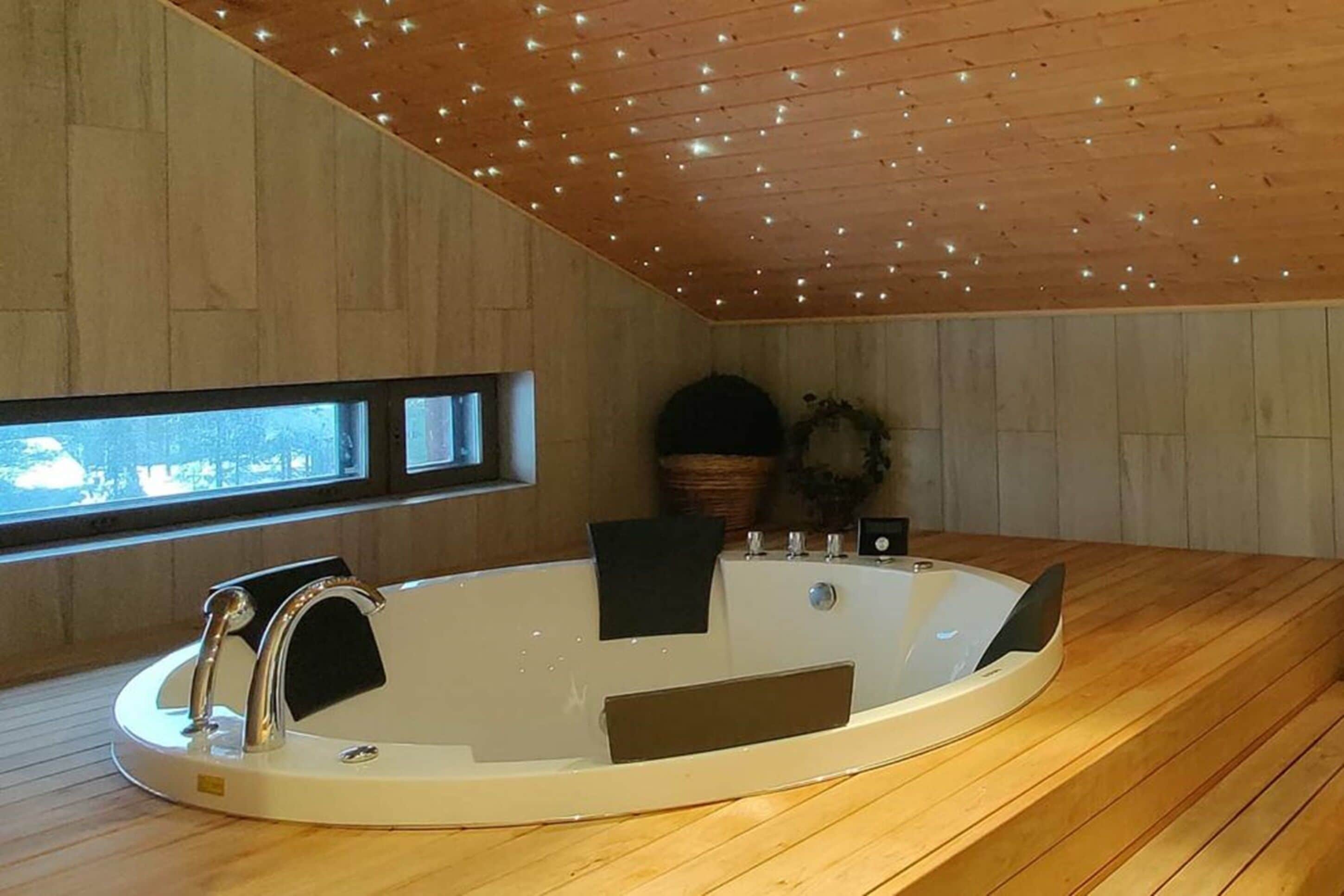A modern bathroom with a freestanding bathtub, wooden flooring, and a sloped ceiling with recessed lighting.