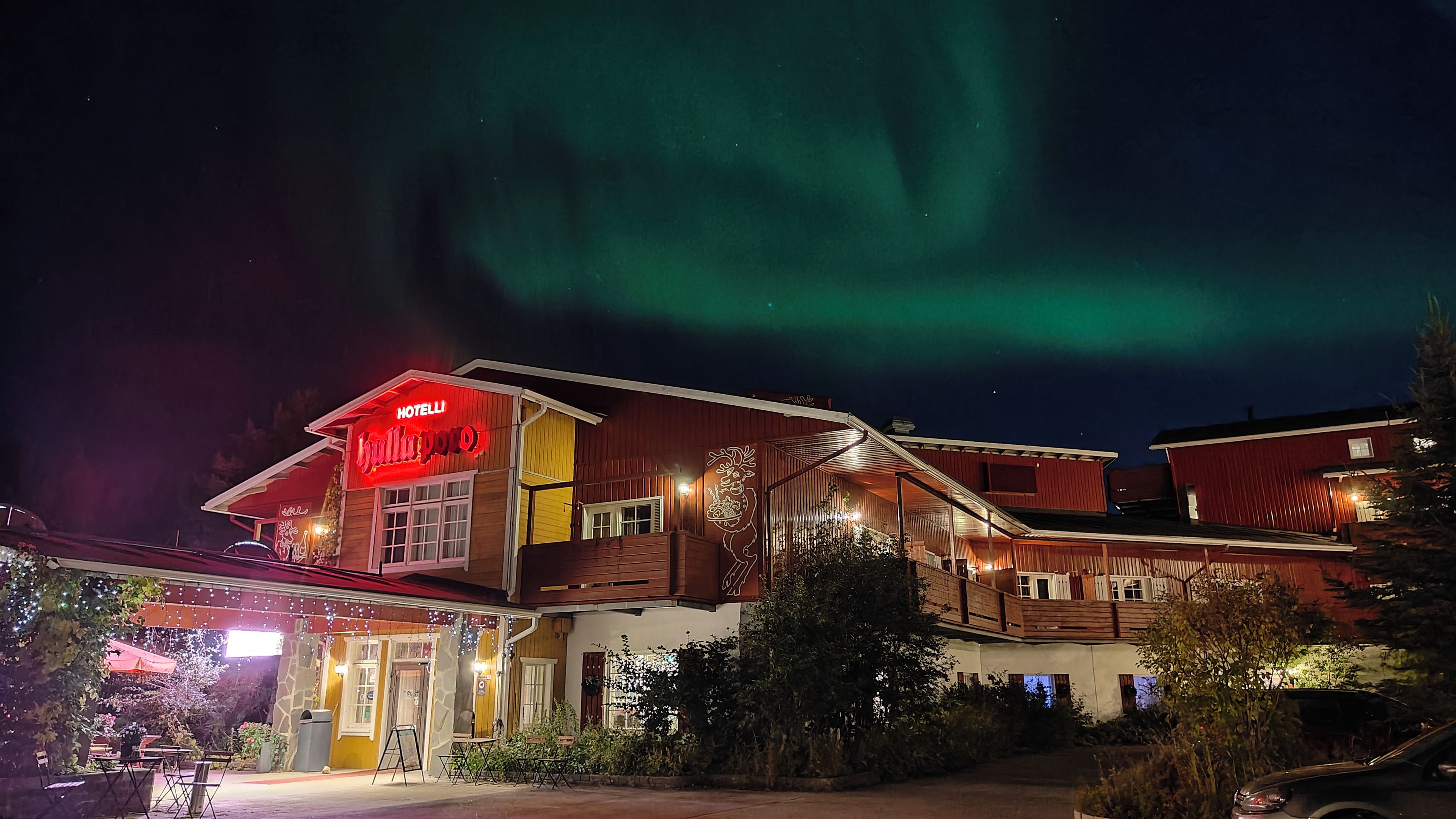 Un hotel con un letrero rojo llamativo, un área de estar al aire libre cubierta y vistas de la aurora boreal.