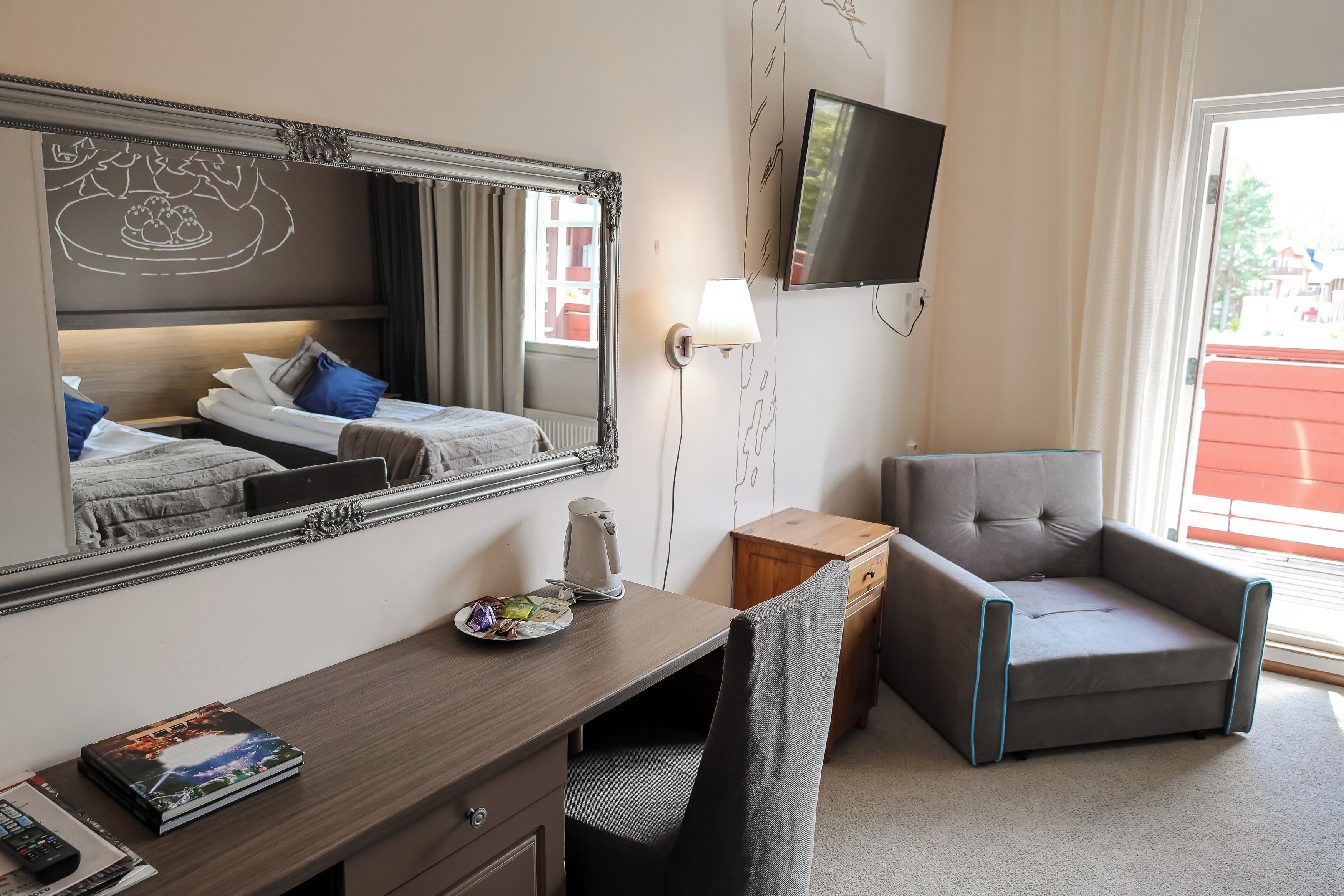 A hotel room with a bed, a desk with a laptop, a chair, a television, and a window with a view.