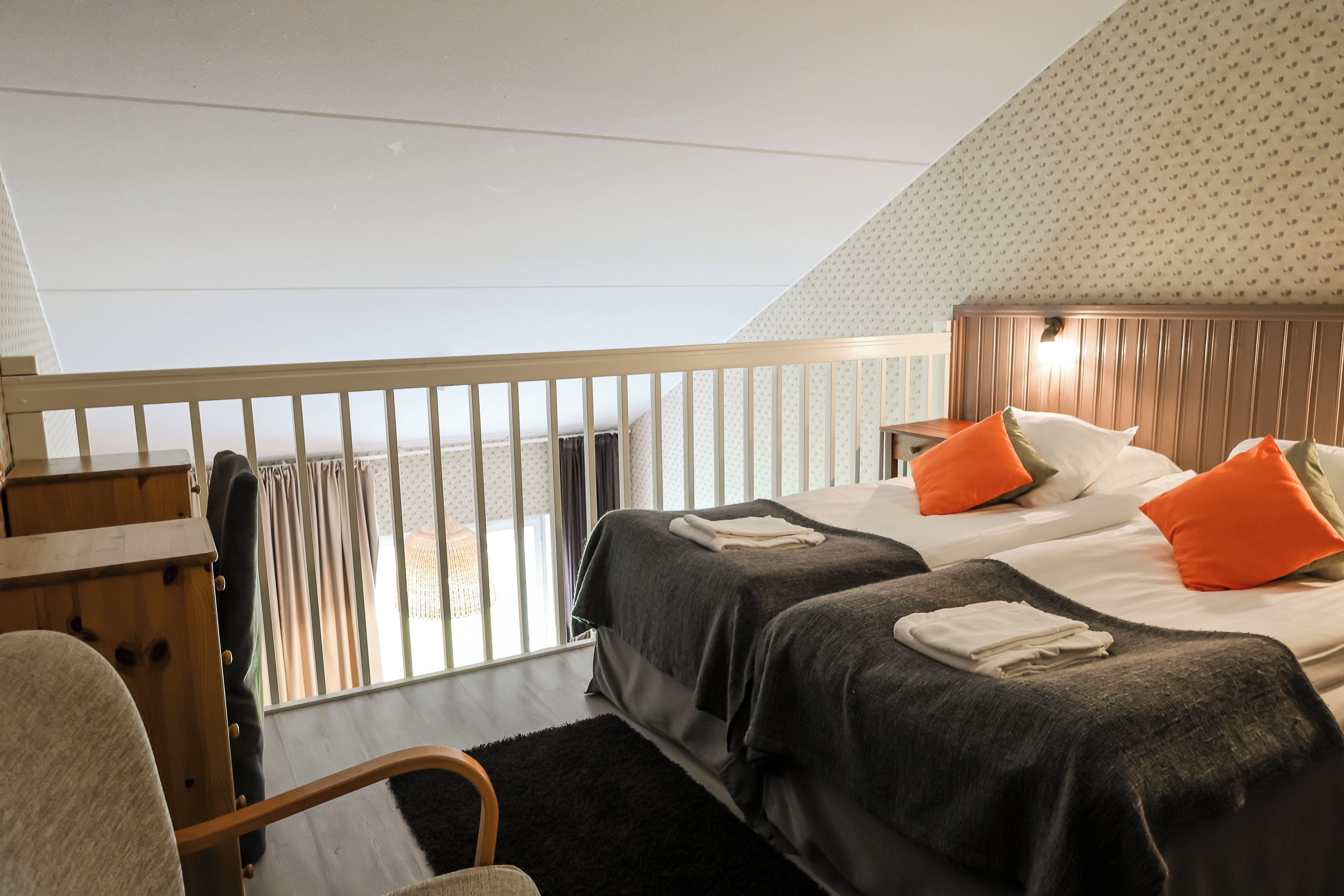 A bedroom with two beds, a wooden headboard, a black rug, and a window with curtains.