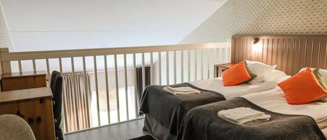 A bedroom with two beds, a wooden headboard, a black rug, and a window with curtains.