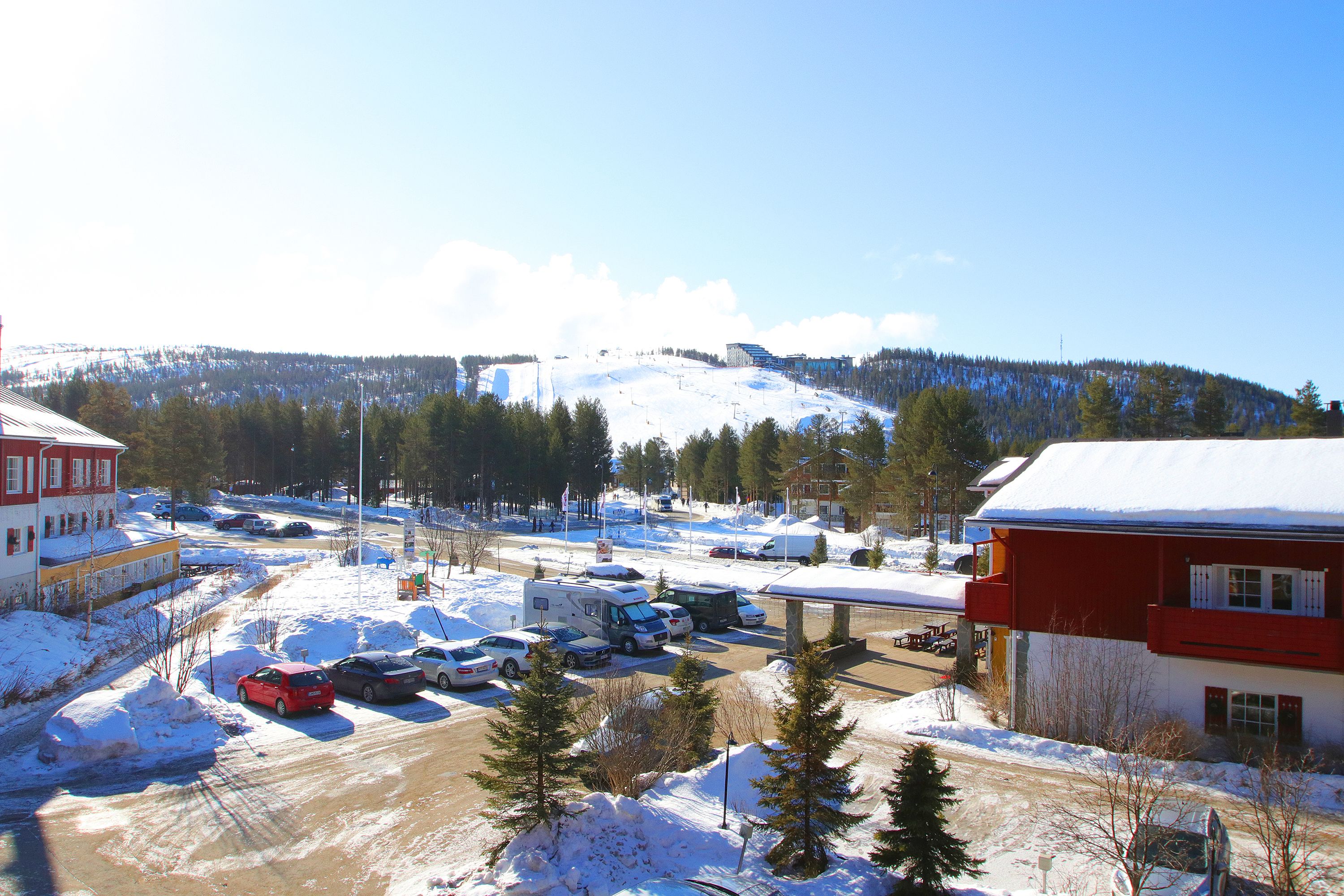 A snowy parking lot with RVs and cars, a building with a red facade, and a mountain in the background.