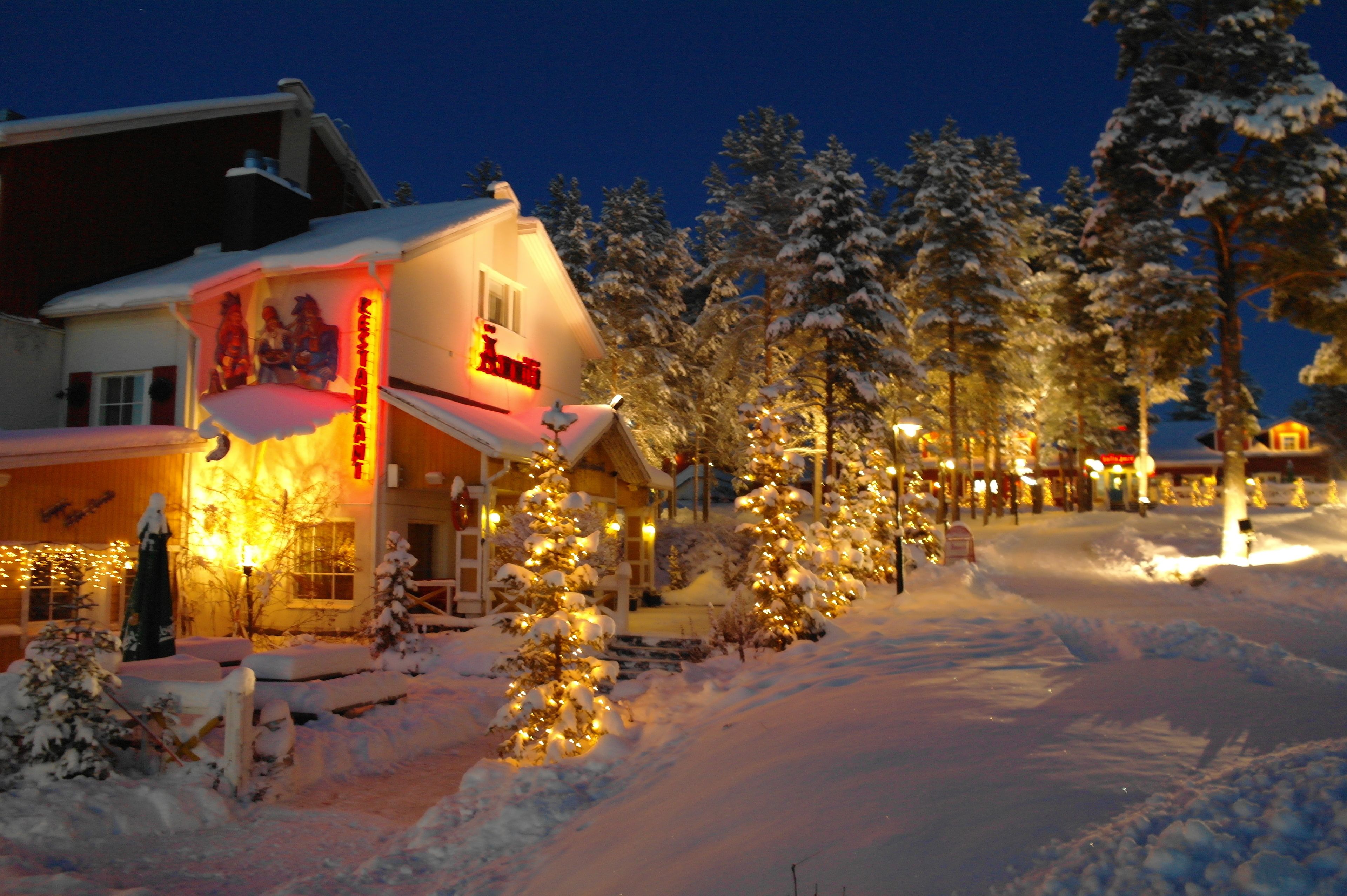A hotel with a snow-covered landscape, illuminated by warm lights, and surrounded by snow-laden trees.