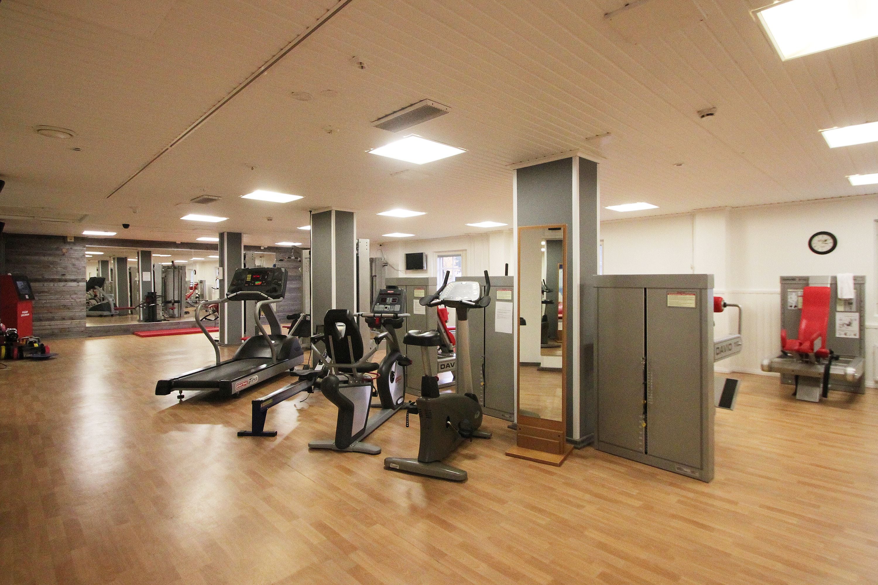 Une salle de sport équipée de divers appareils d’exercice, dotée d’un plancher en bois et d’un mur recouvert de miroirs.