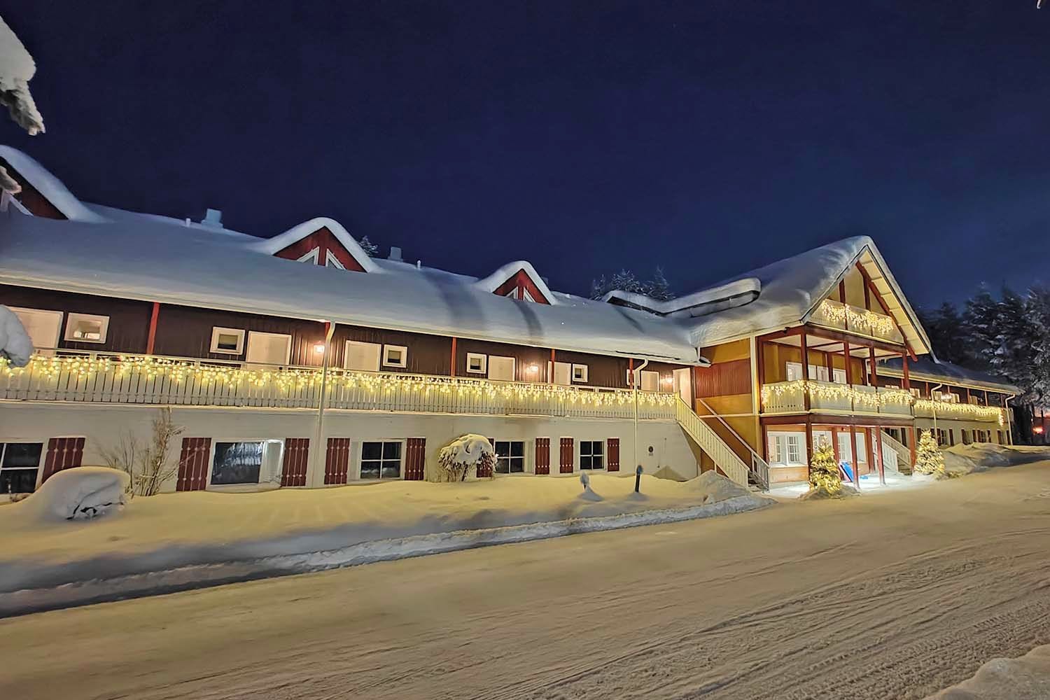 A multi-story hotel with a snow-covered roof and a balcony with string lights.
