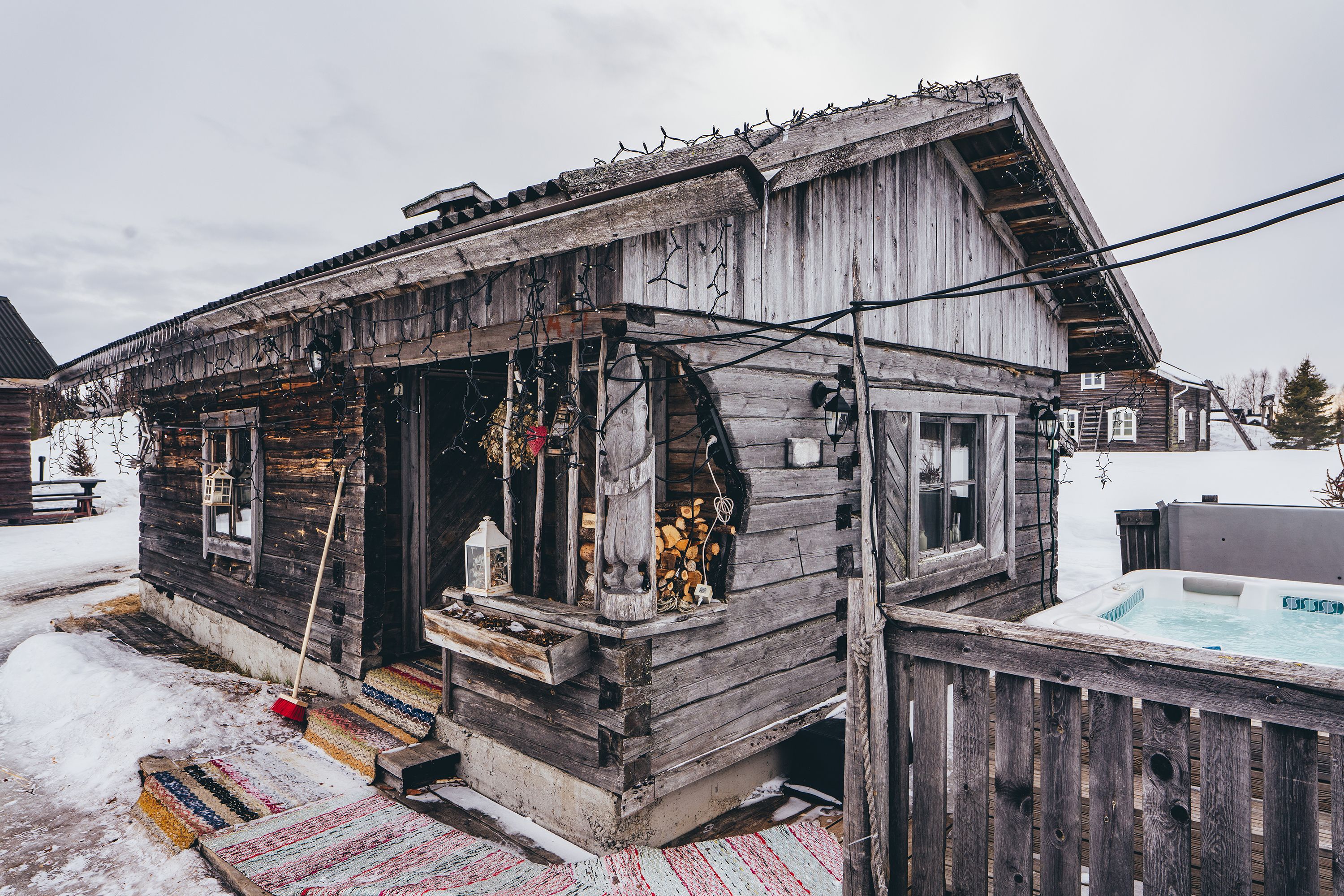A rustic wooden cabin with a porch, a hot tub, and a snow-covered yard.