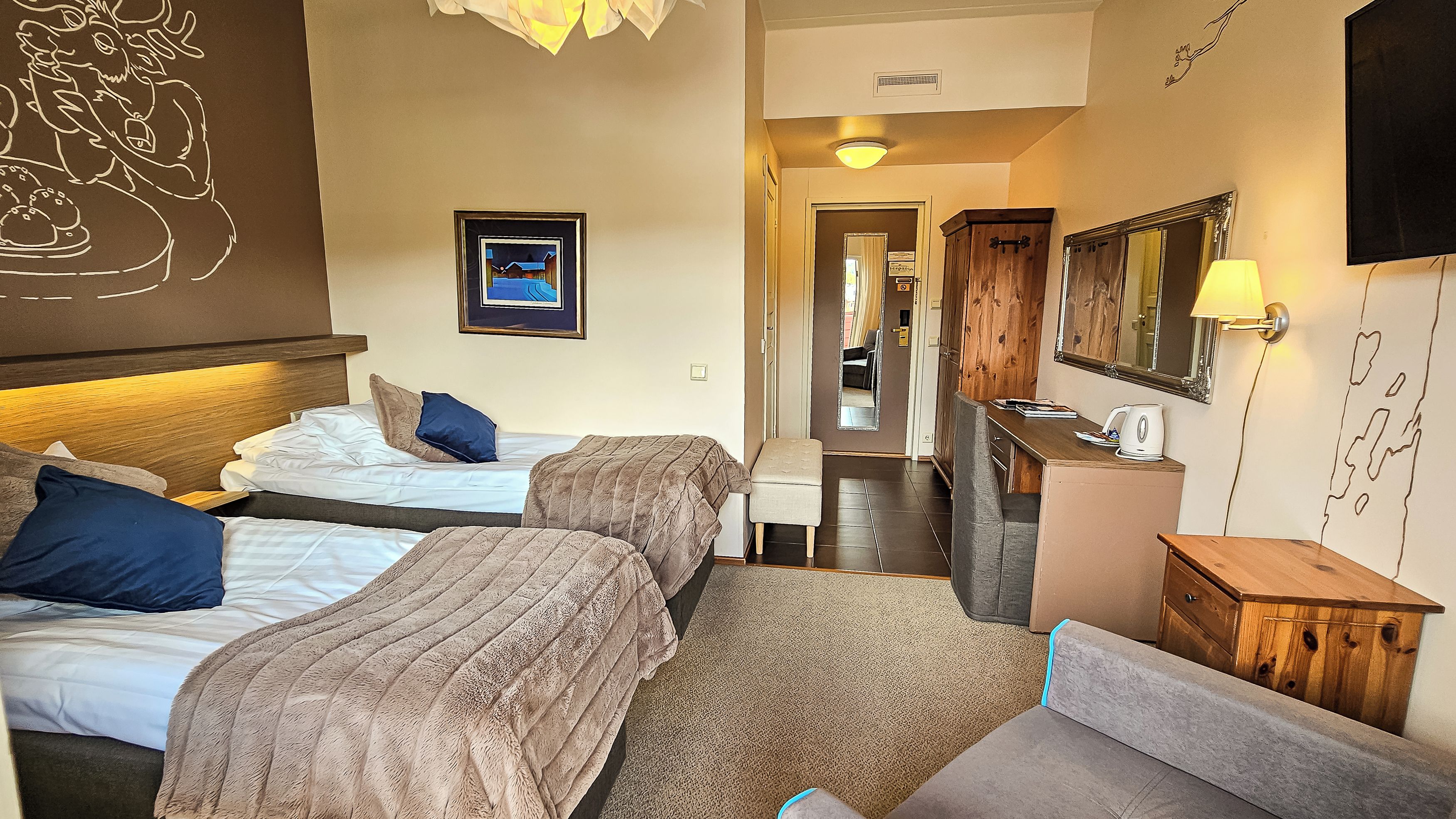 A hotel room with two beds, a desk, a mirror, and a television.