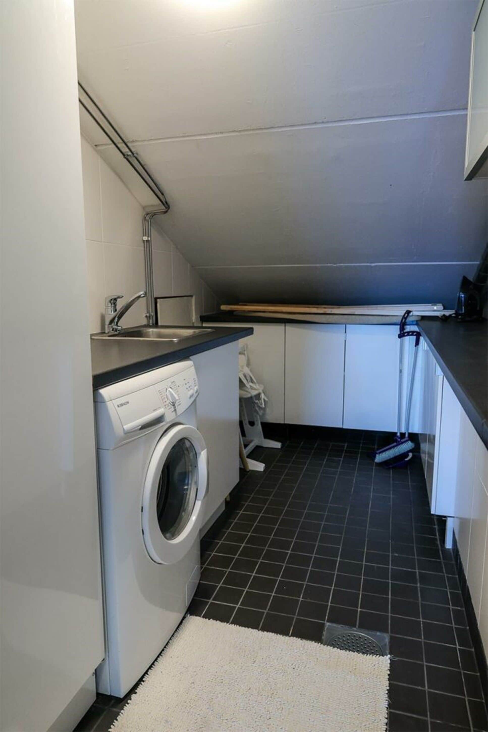 A compact kitchen with a washing machine, a sink, and a broom.