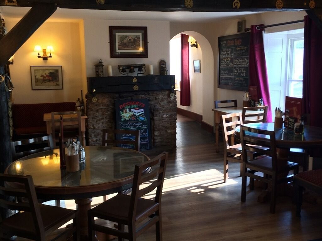 Um restaurante acolhedor com lareira de pedra, mesas e cadeiras de madeira e um menu em lousa.